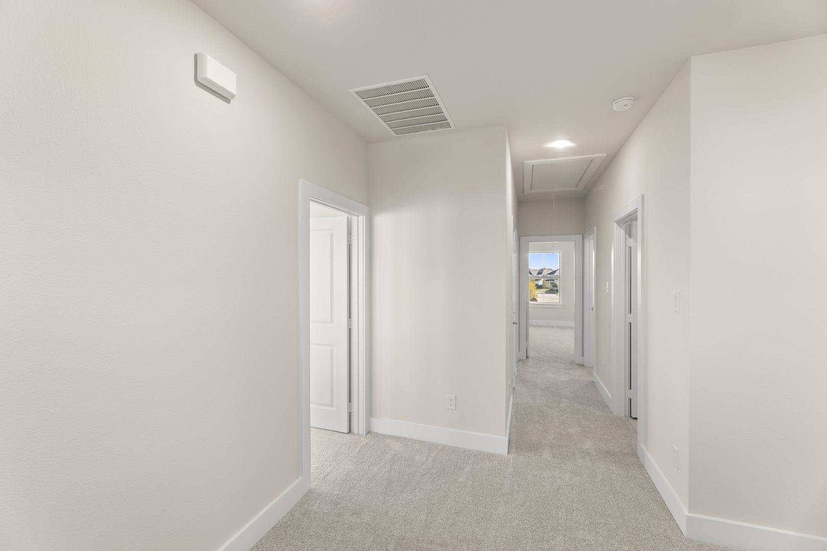 A bright, minimalist hallway with white walls, a carpeted floor, and several doors leading to other rooms.