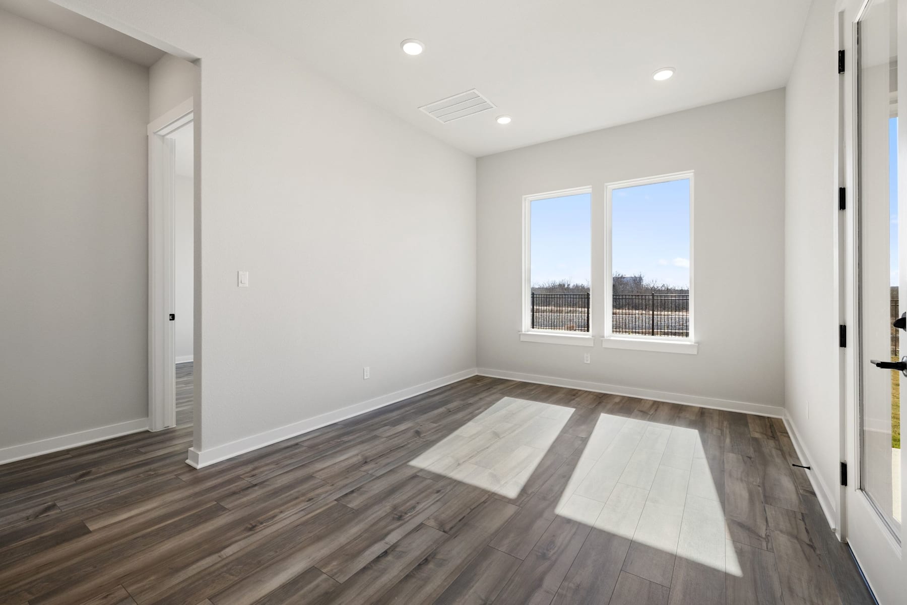 A spacious, well-lit room with a large window overlooking a scenic outdoor view, featuring a hardwood floor with a contrasting pattern.