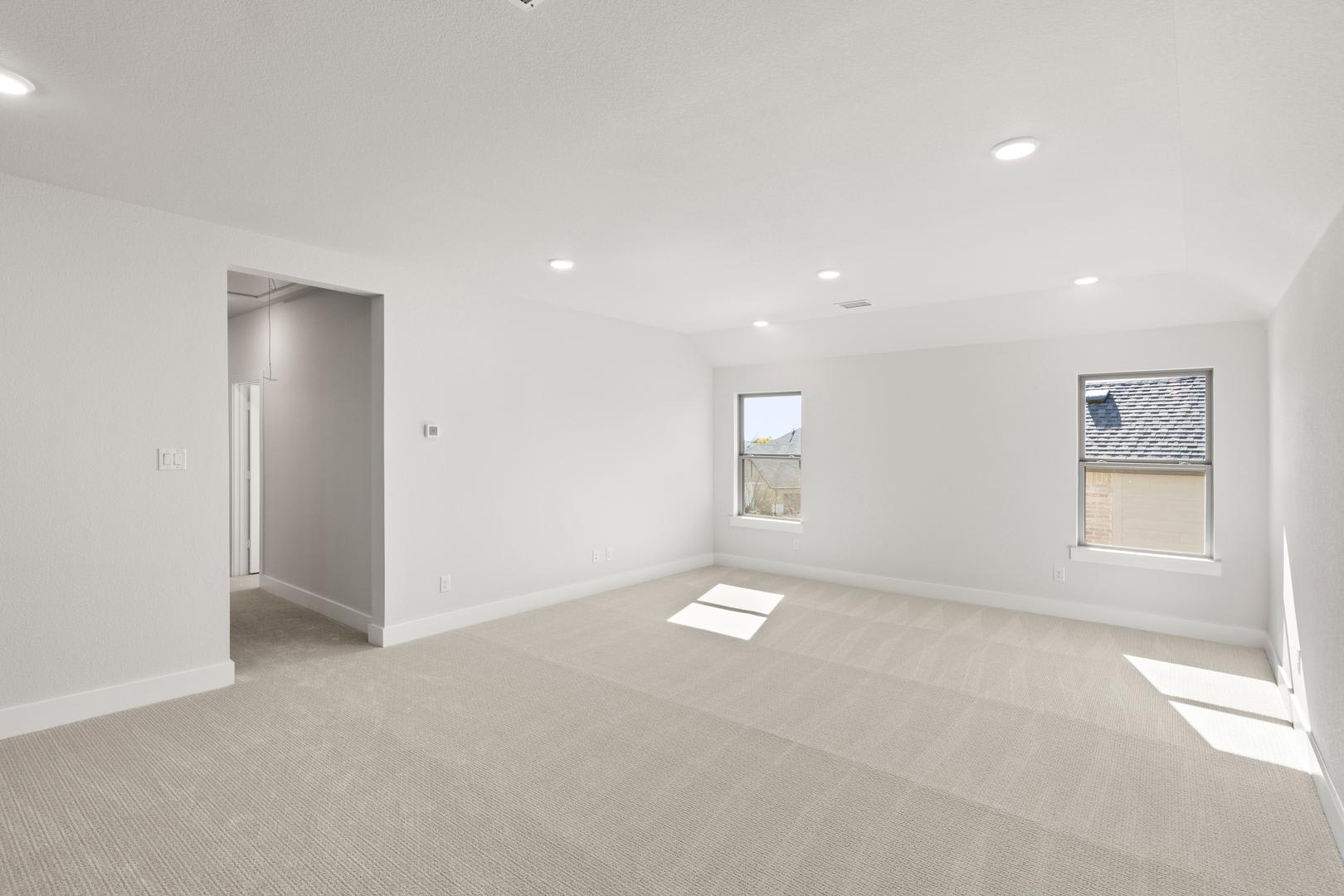 An empty, bright, and spacious room with white walls, a hardwood floor, and recessed lighting.