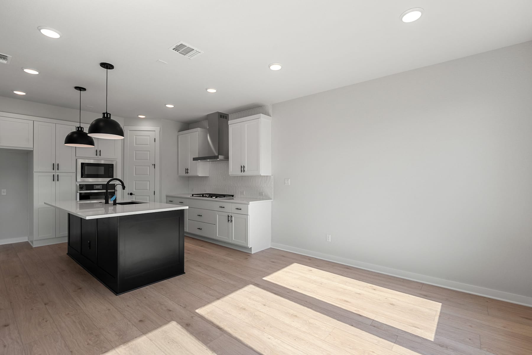 A modern, open-concept kitchen with white cabinets, a black island, and hardwood floors, bathed in natural light from the windows.