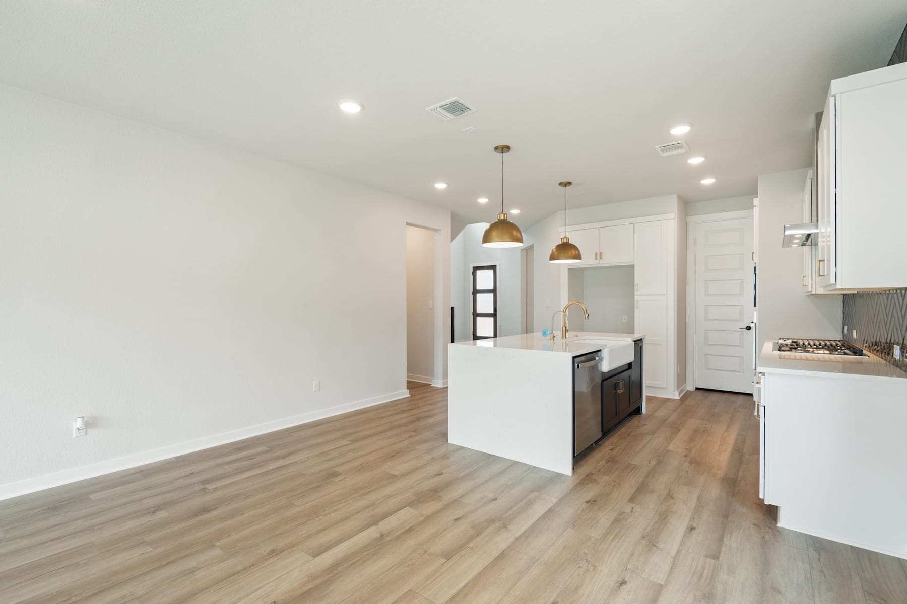 A modern, open-concept kitchen and living space with light-colored hardwood floors, white walls, and pendant lighting fixtures.