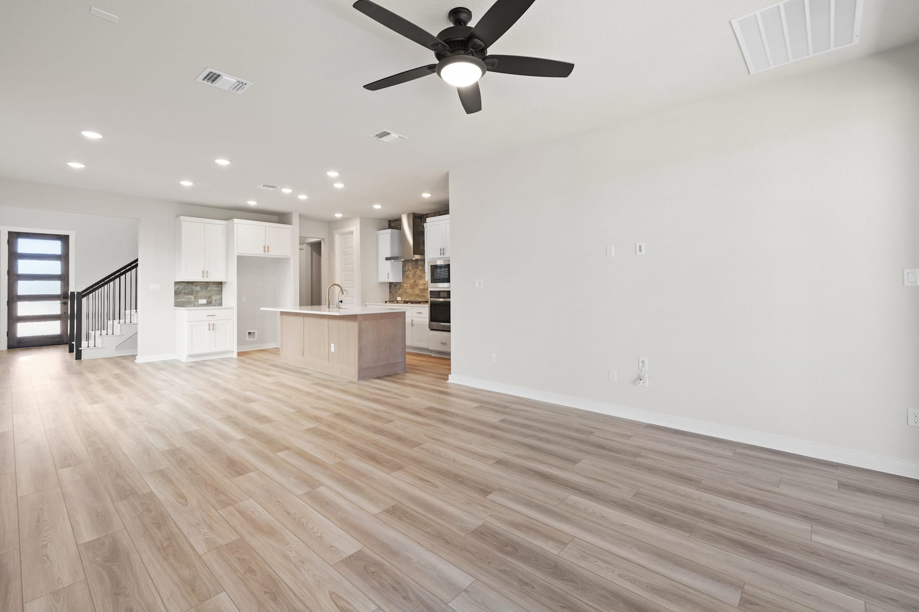A spacious, open-concept living area with a modern kitchen, hardwood floors, and a ceiling fan providing airflow.