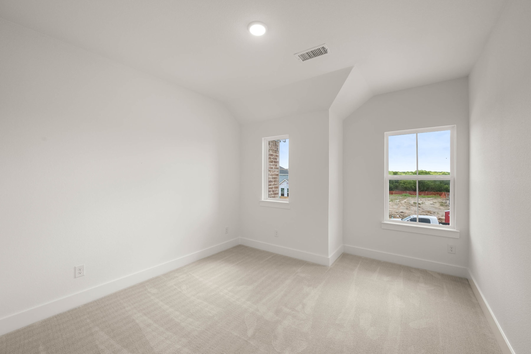 A bright, empty room with white walls, a hardwood floor, and two windows overlooking a scenic outdoor landscape.