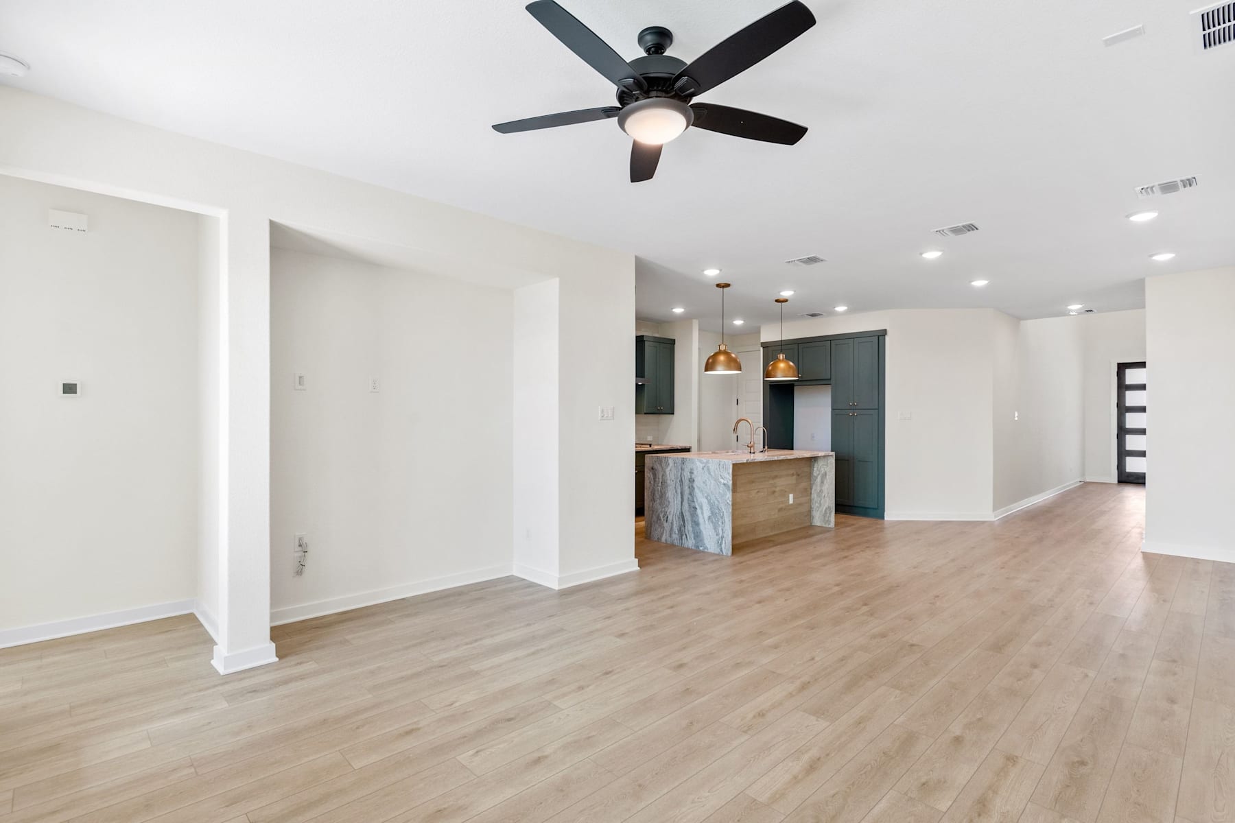A spacious, open-concept living area with a ceiling fan, hardwood floors, and a partially visible kitchen in the background.