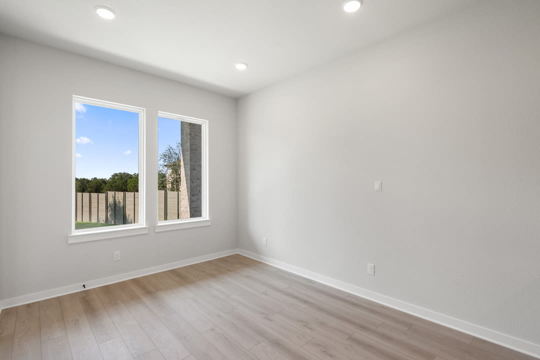 A bright, empty room with large windows overlooking a grassy outdoor area.