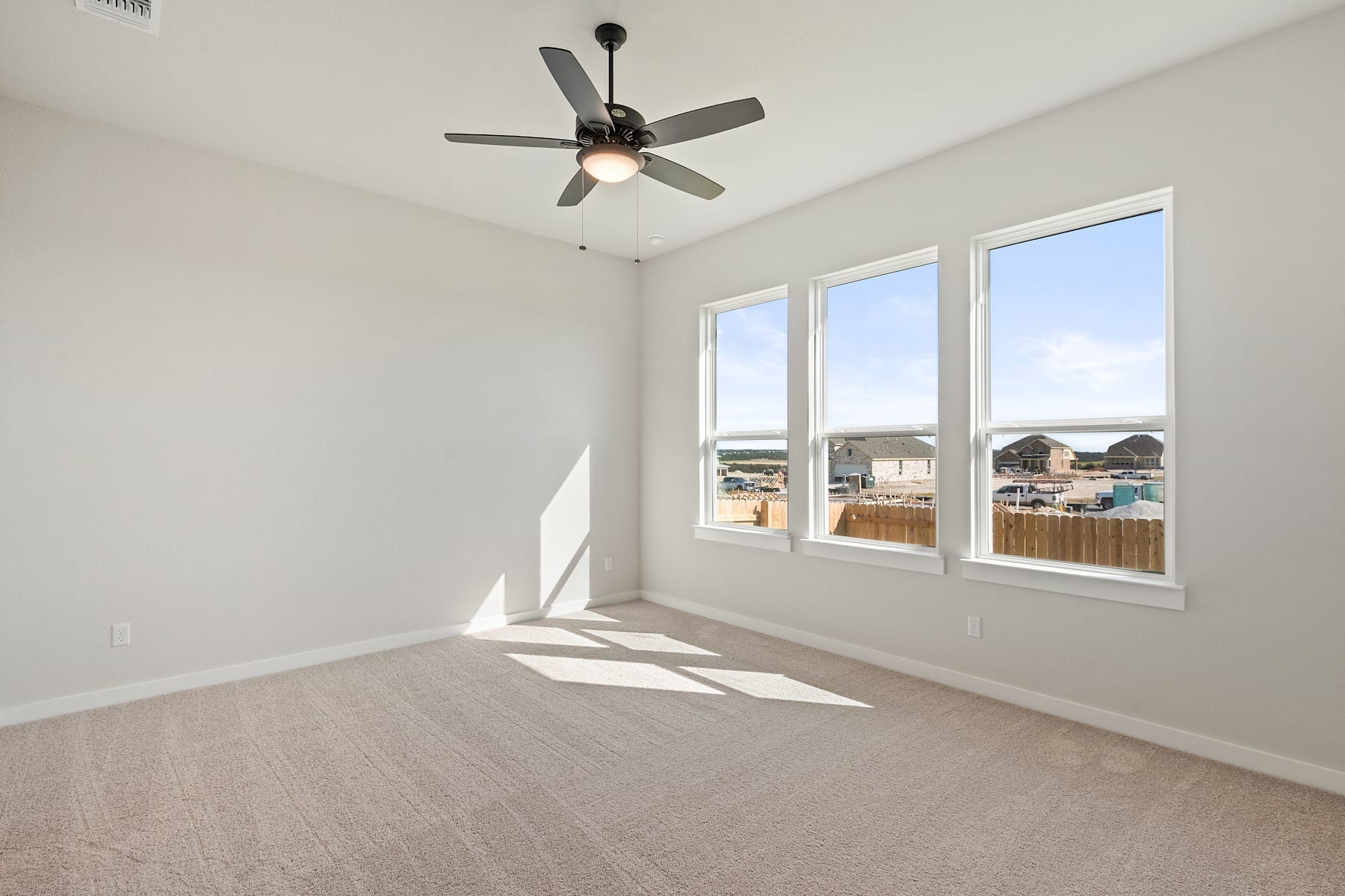 A bright and airy room with a ceiling fan, large windows, and a hardwood floor, providing a view of the outdoor scenery.