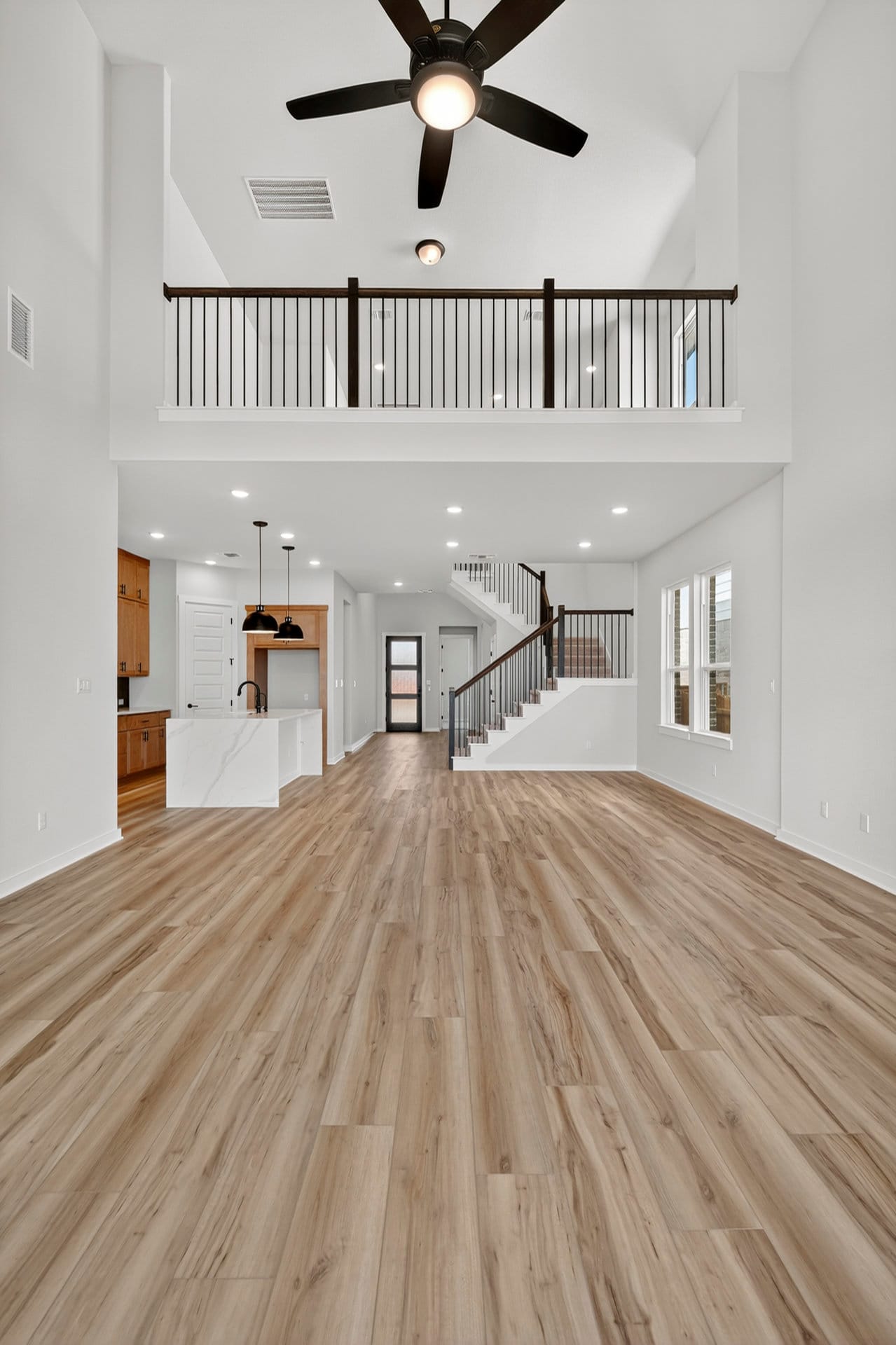 A spacious and modern open-plan living area with a wooden floor, a ceiling fan, and a staircase leading to an upper level.