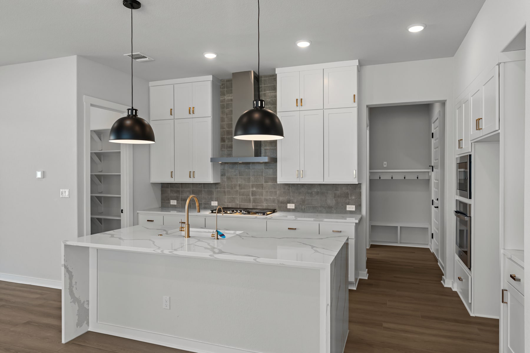 A modern, bright kitchen with white cabinets, a marble countertop, and pendant lights hanging above the island.