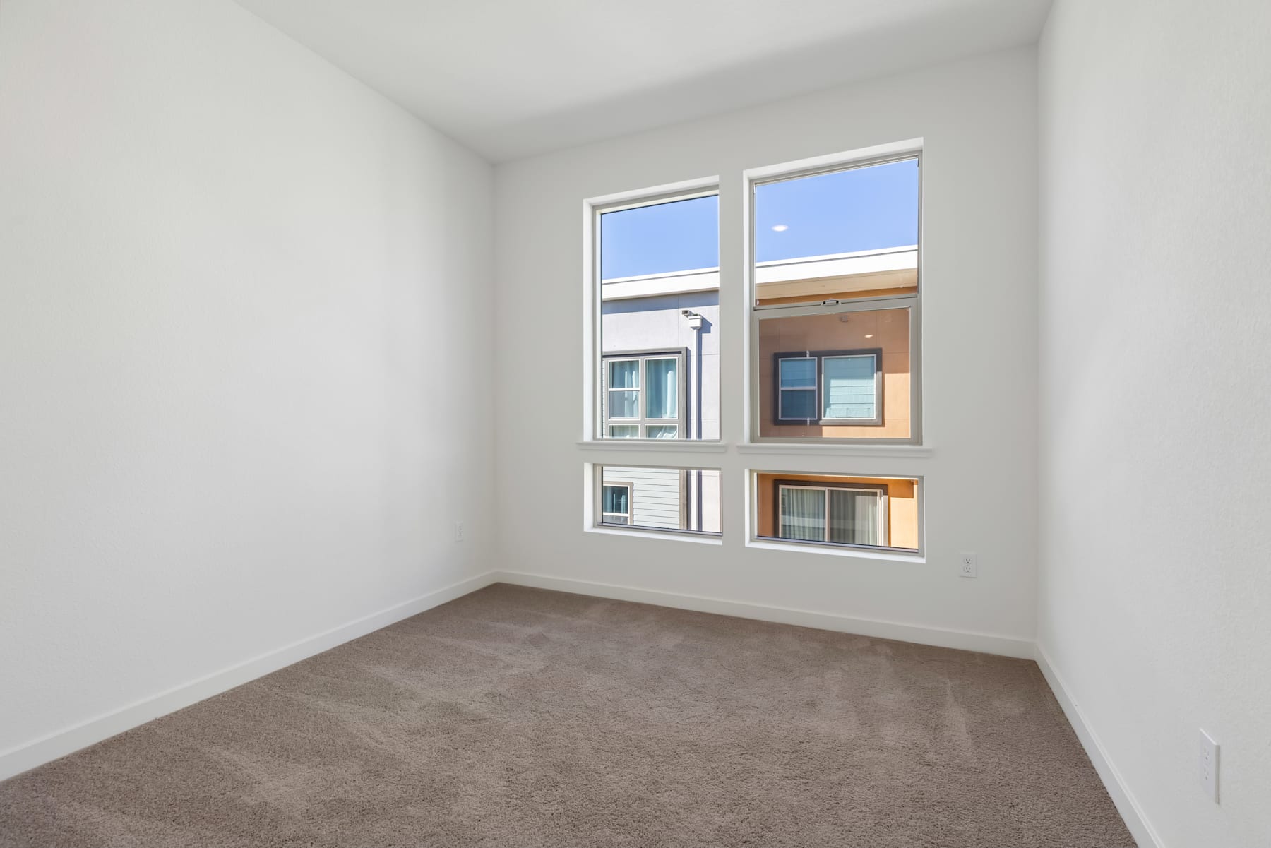 A spacious, well-lit room with large windows, a neutral-colored carpet, and a clean, minimalist interior design.