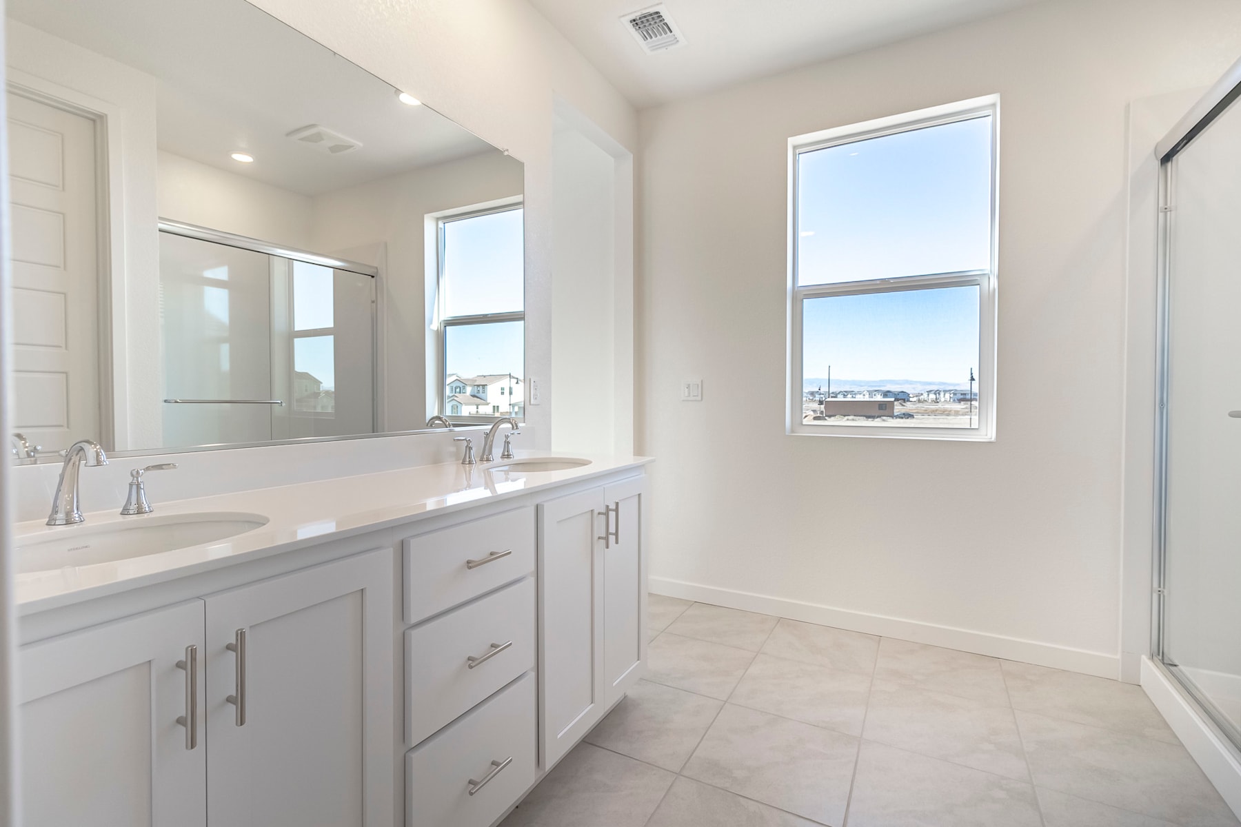 A bright and spacious bathroom with white cabinets, a large mirror, and a view of the city through the window.