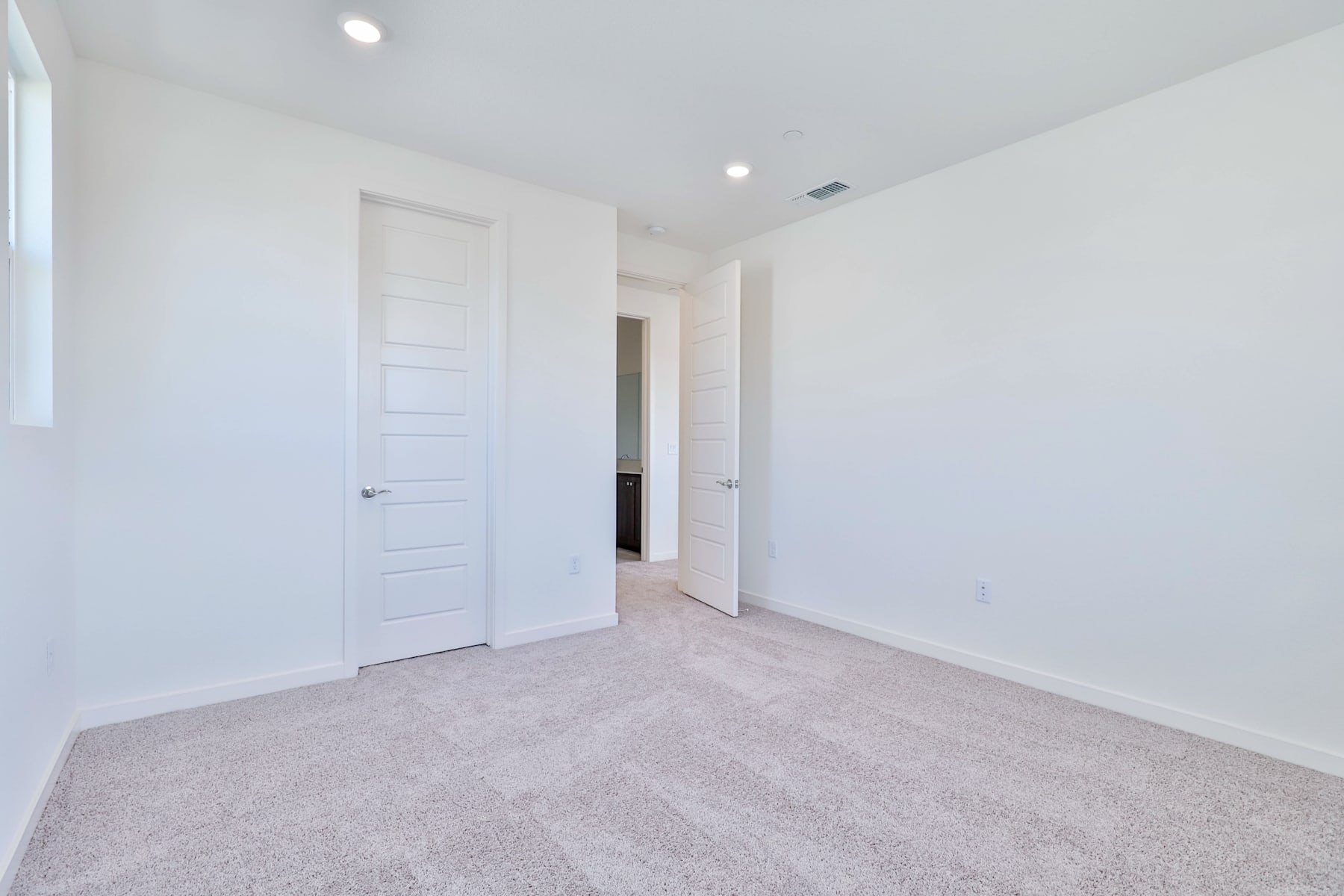 A spacious, minimalist room with white walls, a carpeted floor, and a closed door leading to another area.
