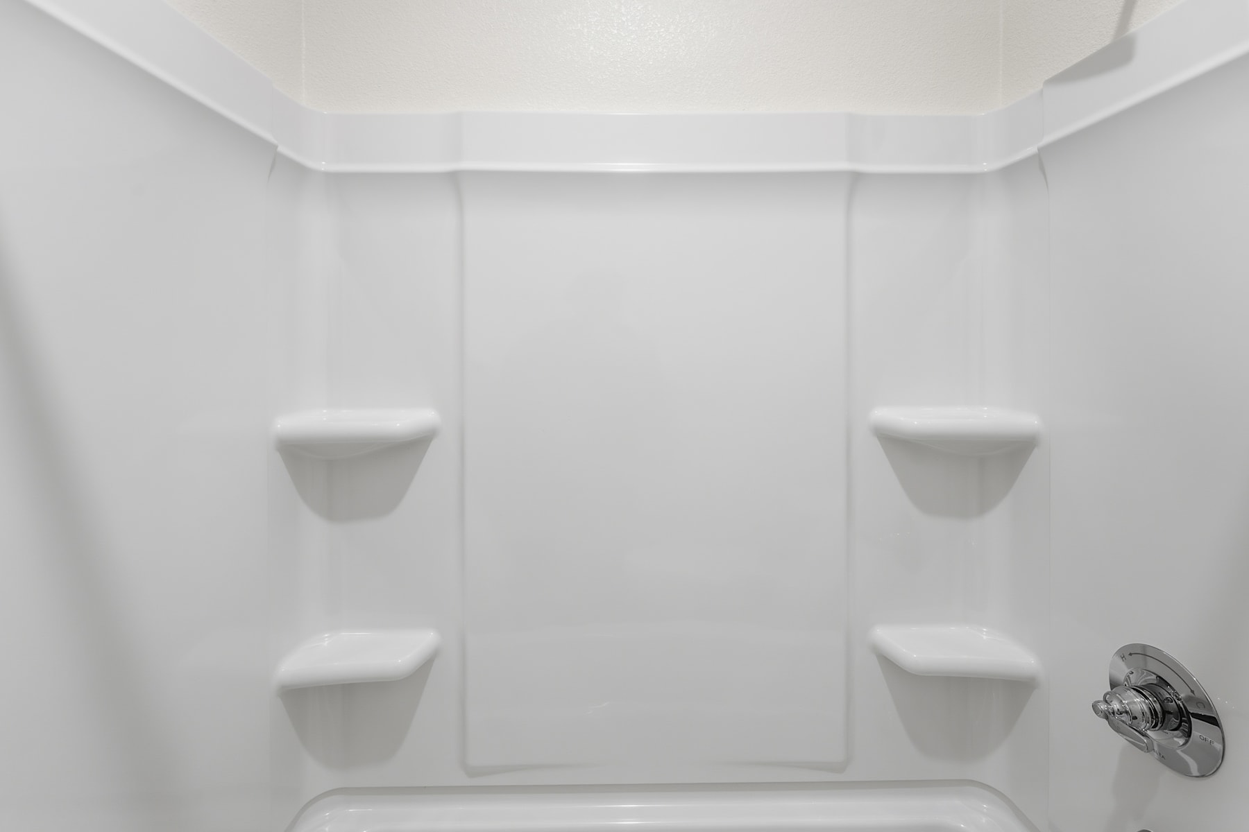 A simple, minimalist bathroom interior with white walls, a shower stall, and a recessed shelf on either side.