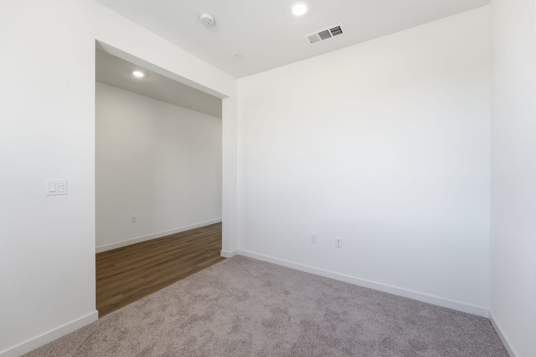 A spacious, minimalist room with white walls, a hardwood floor, and a doorway leading to another area.