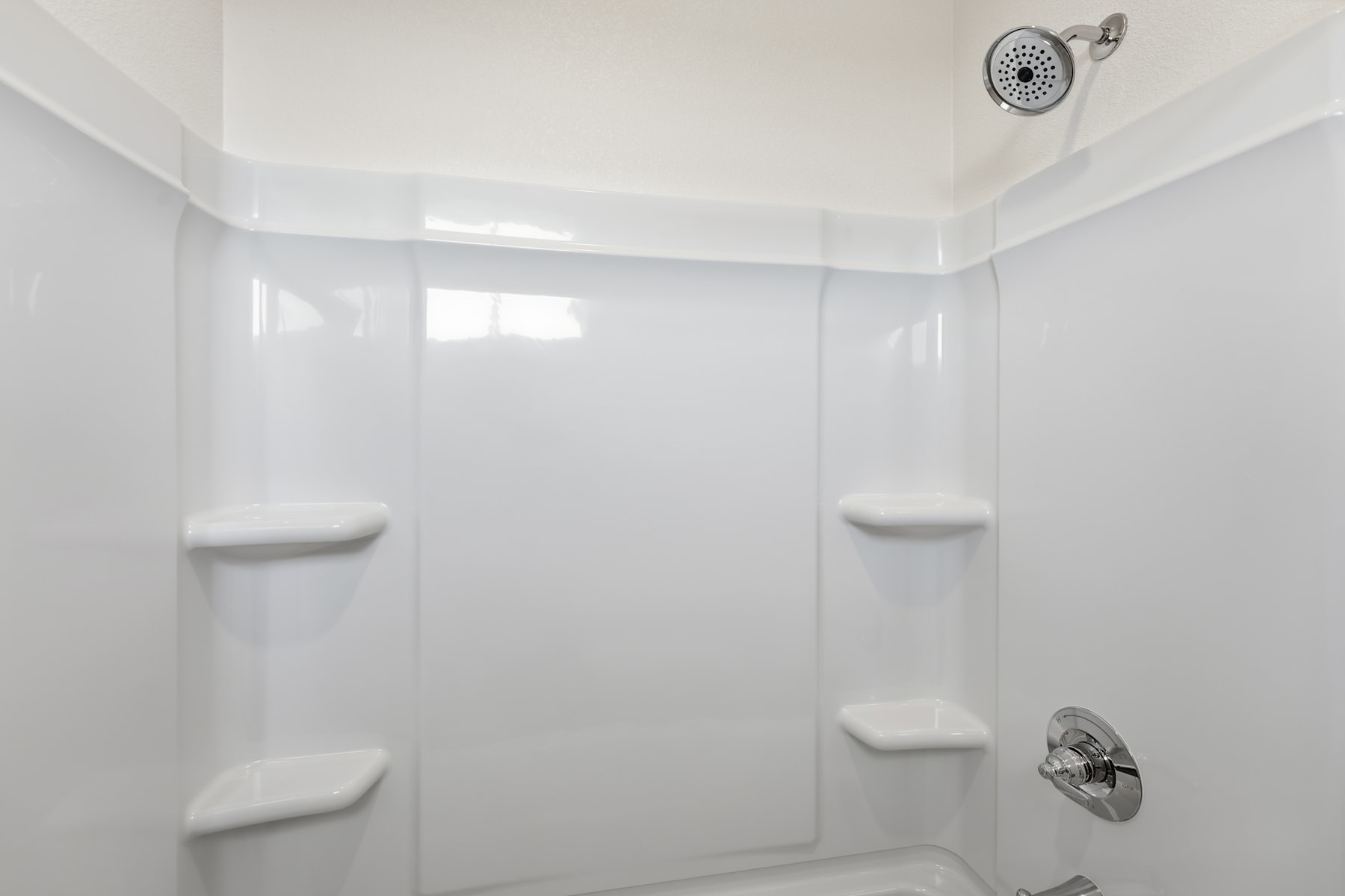 A bright, minimalist bathroom with white walls, a shower head, and built-in shelves.