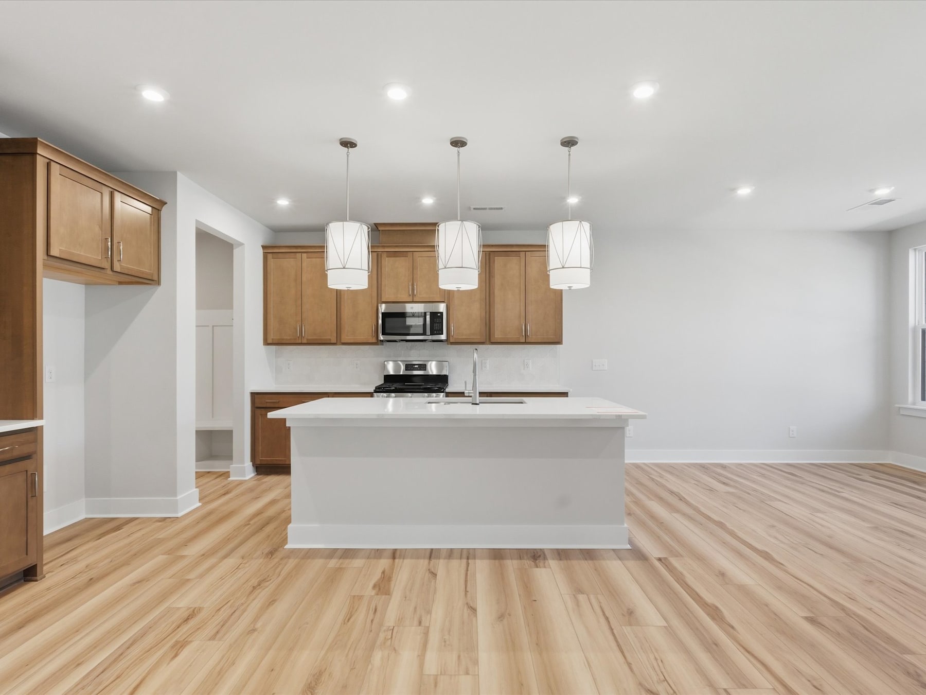 A modern, open-concept kitchen with light wood cabinets, a white island, and hardwood floors, illuminated by pendant lights.