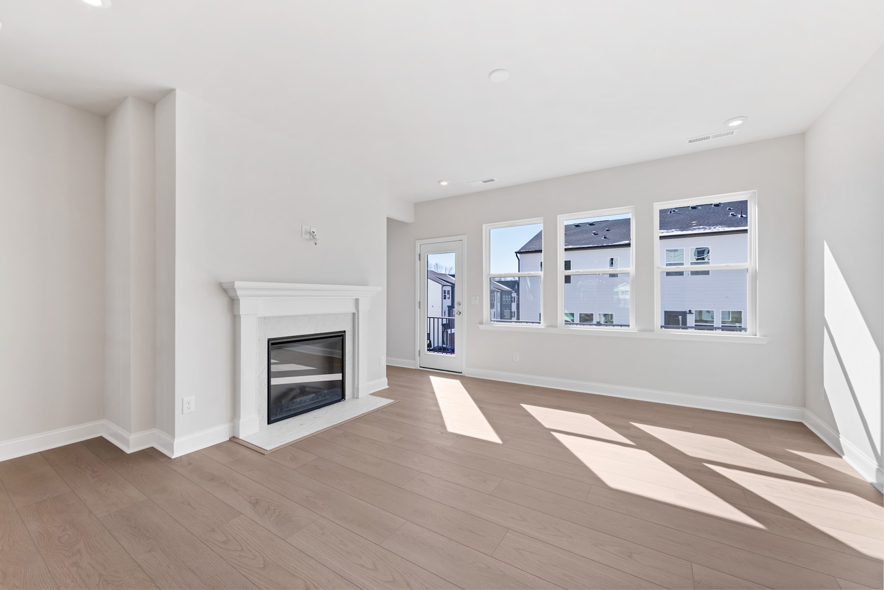 A bright and spacious room with a fireplace and large windows overlooking the exterior, featuring hardwood floors and a minimalist design.