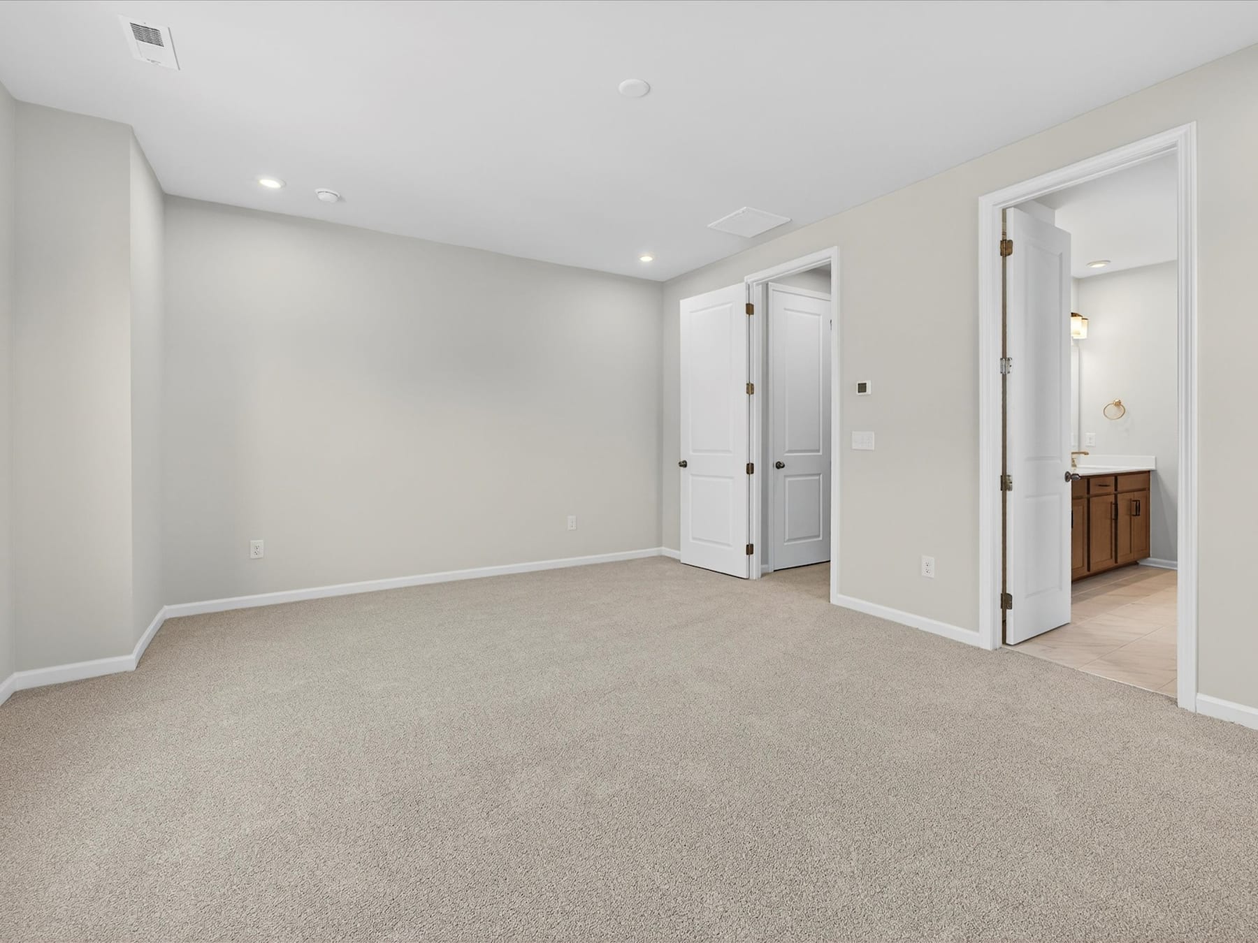 A spacious, well-lit room with neutral-colored walls and carpeted flooring, featuring a doorway leading to another room.