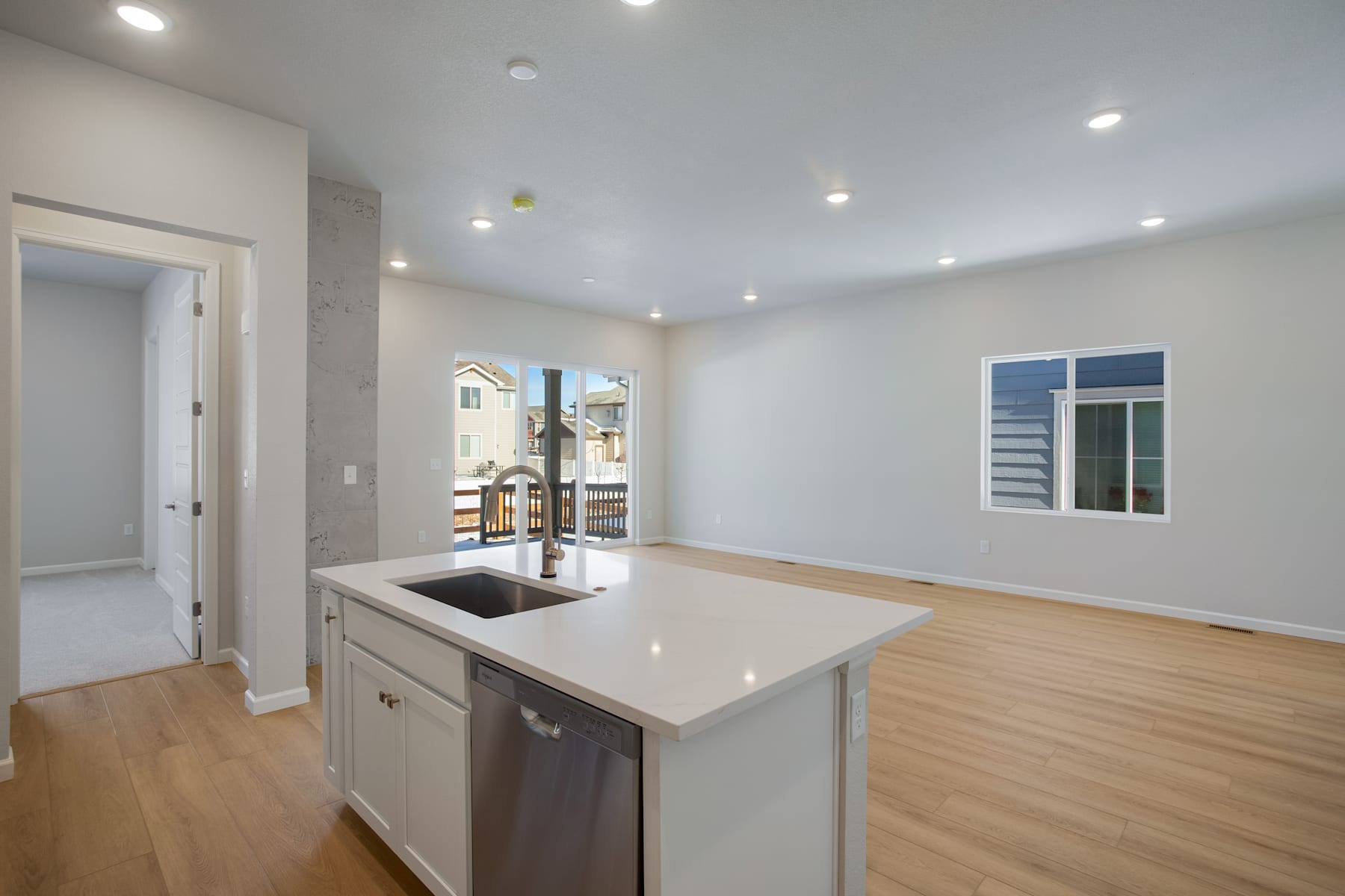 A modern, open-concept kitchen with white cabinets, a sleek countertop, and hardwood flooring, leading into a bright and airy living space with large windows.