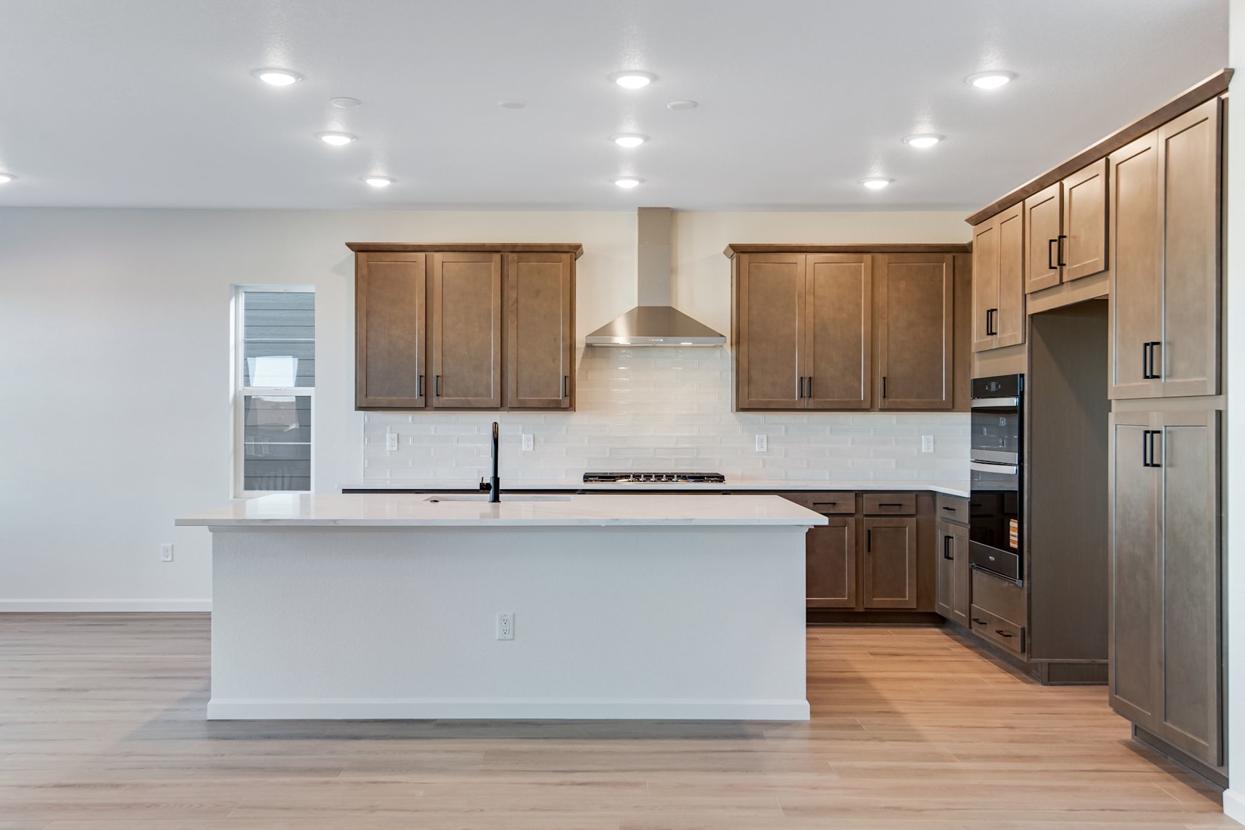 A modern kitchen with wooden cabinets, a white island, and stainless steel appliances, set against a bright and airy background.