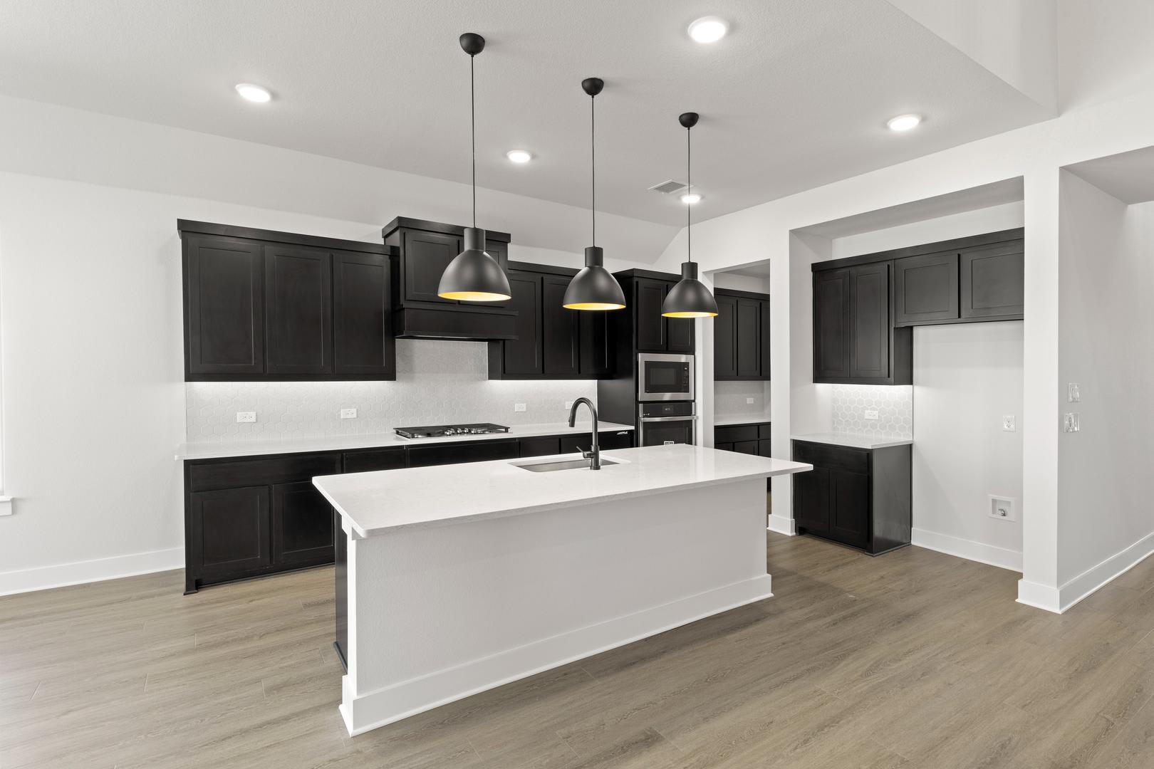 A modern, minimalist kitchen with dark cabinets, a white island, and pendant lights hanging from the ceiling.