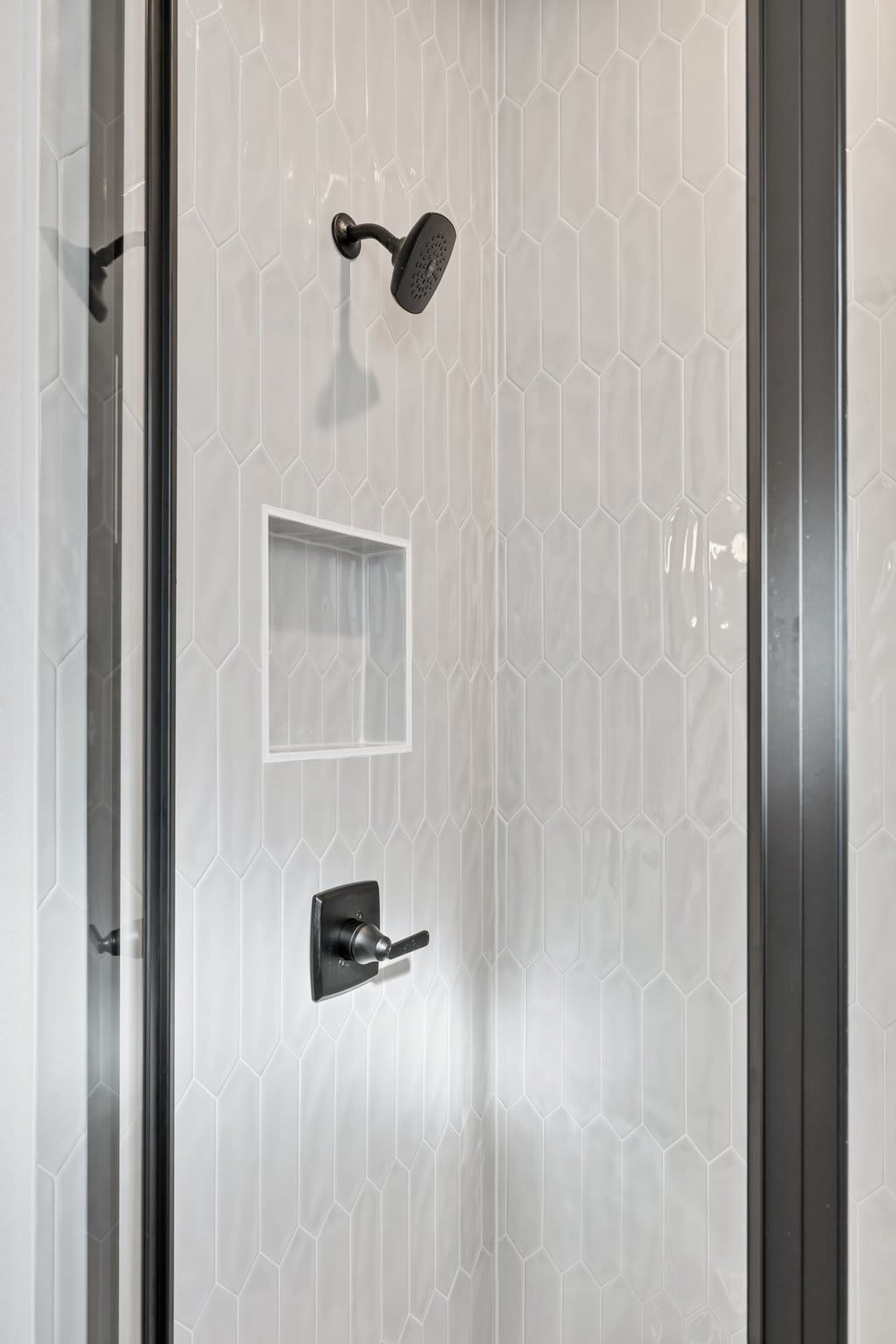 A modern, minimalist shower enclosure with a black shower head and faucet fixtures against a tiled wall.
