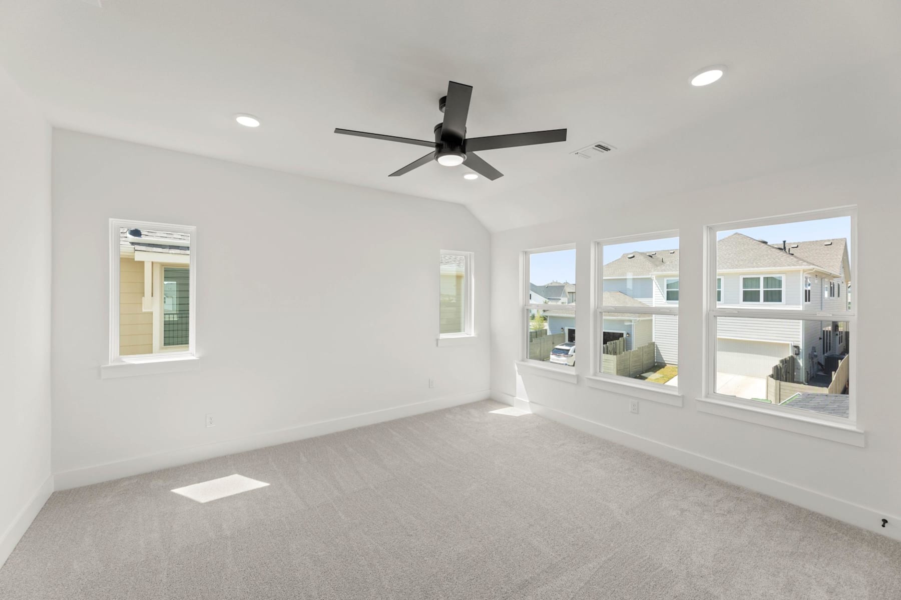 A spacious, well-lit room with a modern ceiling fan and large windows providing a view of the exterior.