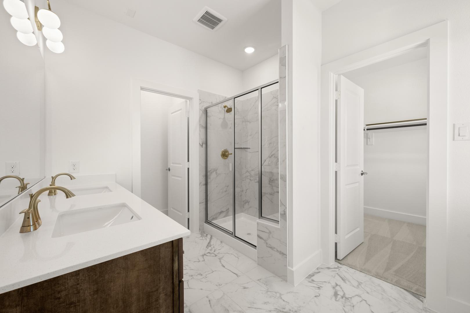 A modern, well-lit bathroom with a marble vanity, a glass-enclosed shower, and a chandelier overhead, creating a luxurious and inviting atmosphere.