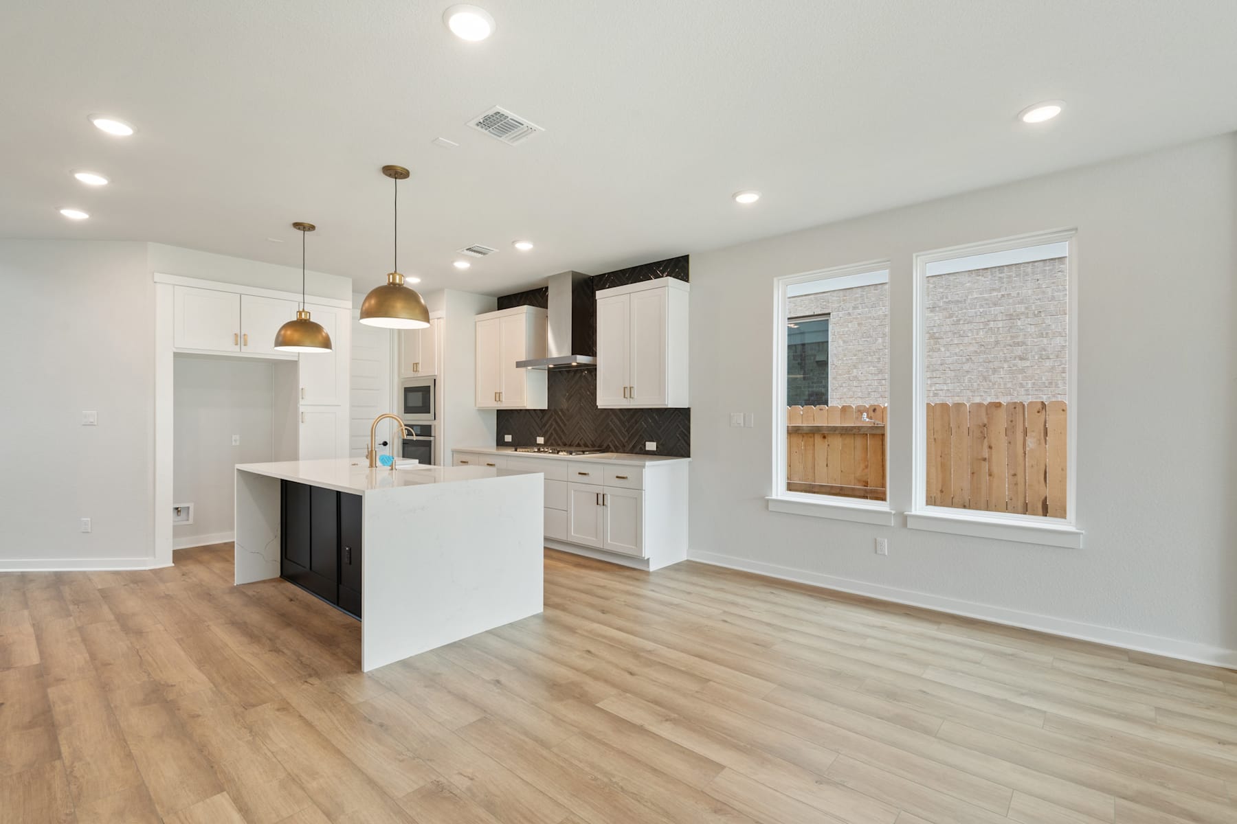 A modern, open-concept kitchen with white cabinets, wooden floors, and pendant lighting, leading into a bright and airy living space.