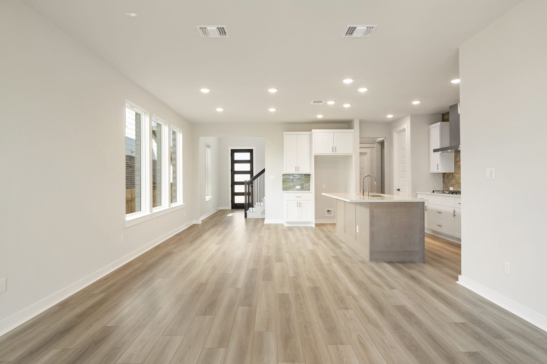A spacious and modern kitchen with white cabinets, hardwood floors, and recessed lighting, leading into an open living area.