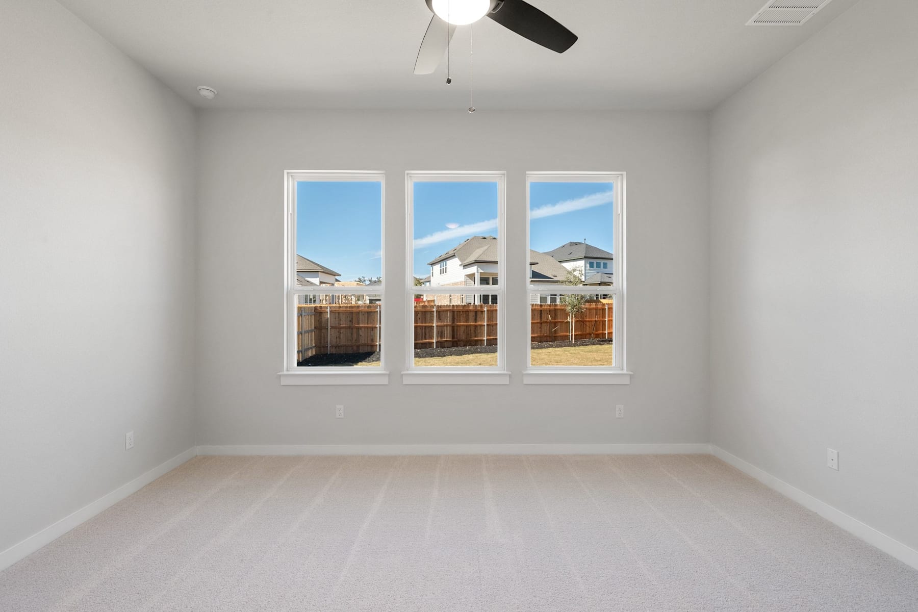 A bright, empty room with large windows overlooking a residential neighborhood in the background.