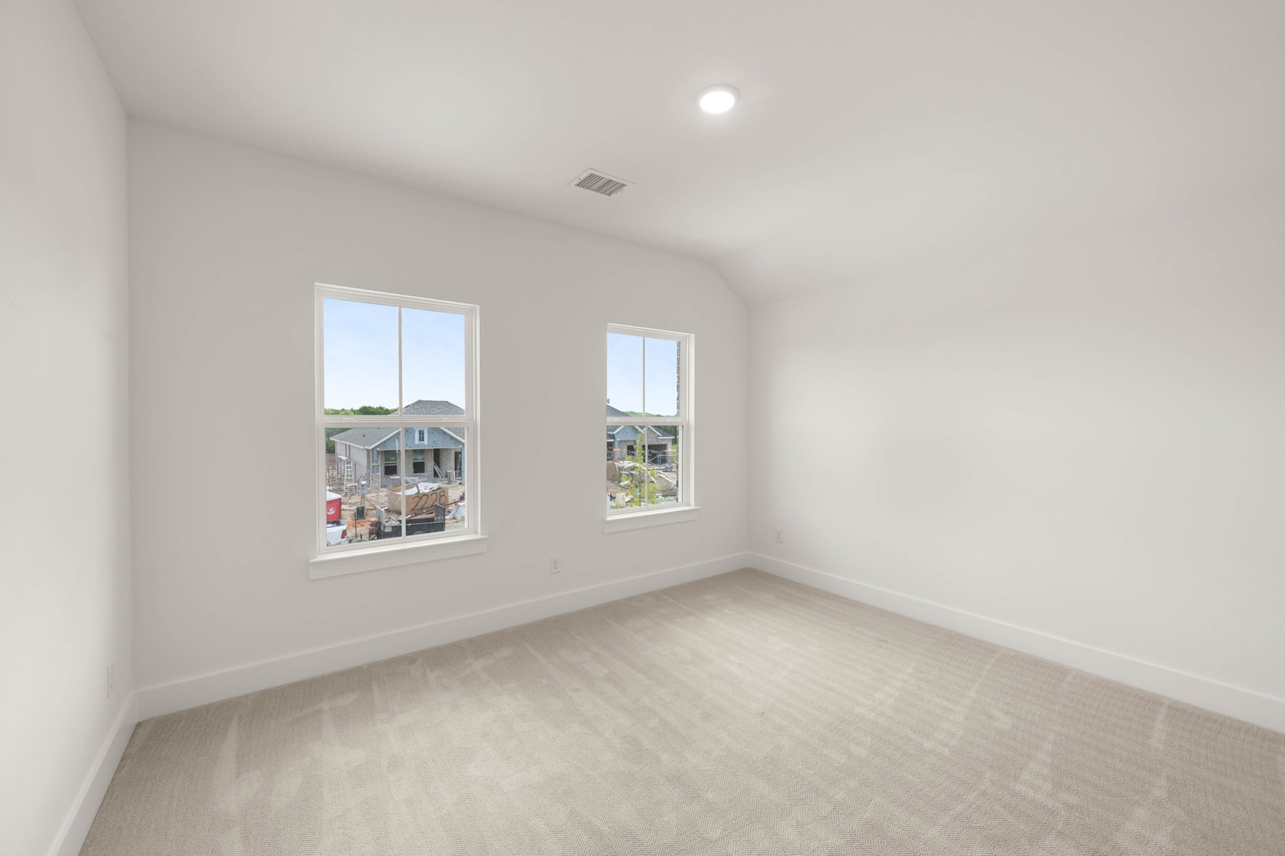 A bright, spacious room with large windows overlooking a residential neighborhood, featuring a clean, minimalist design with hardwood flooring.