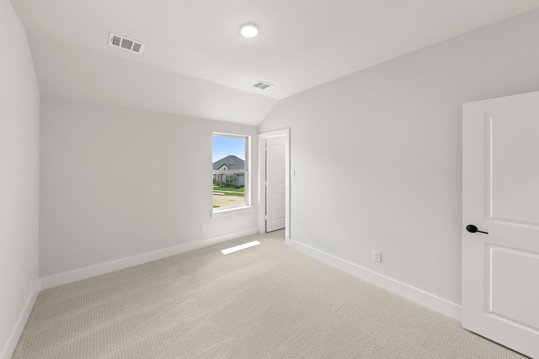 A bright, empty room with a window overlooking a residential neighborhood in the background.