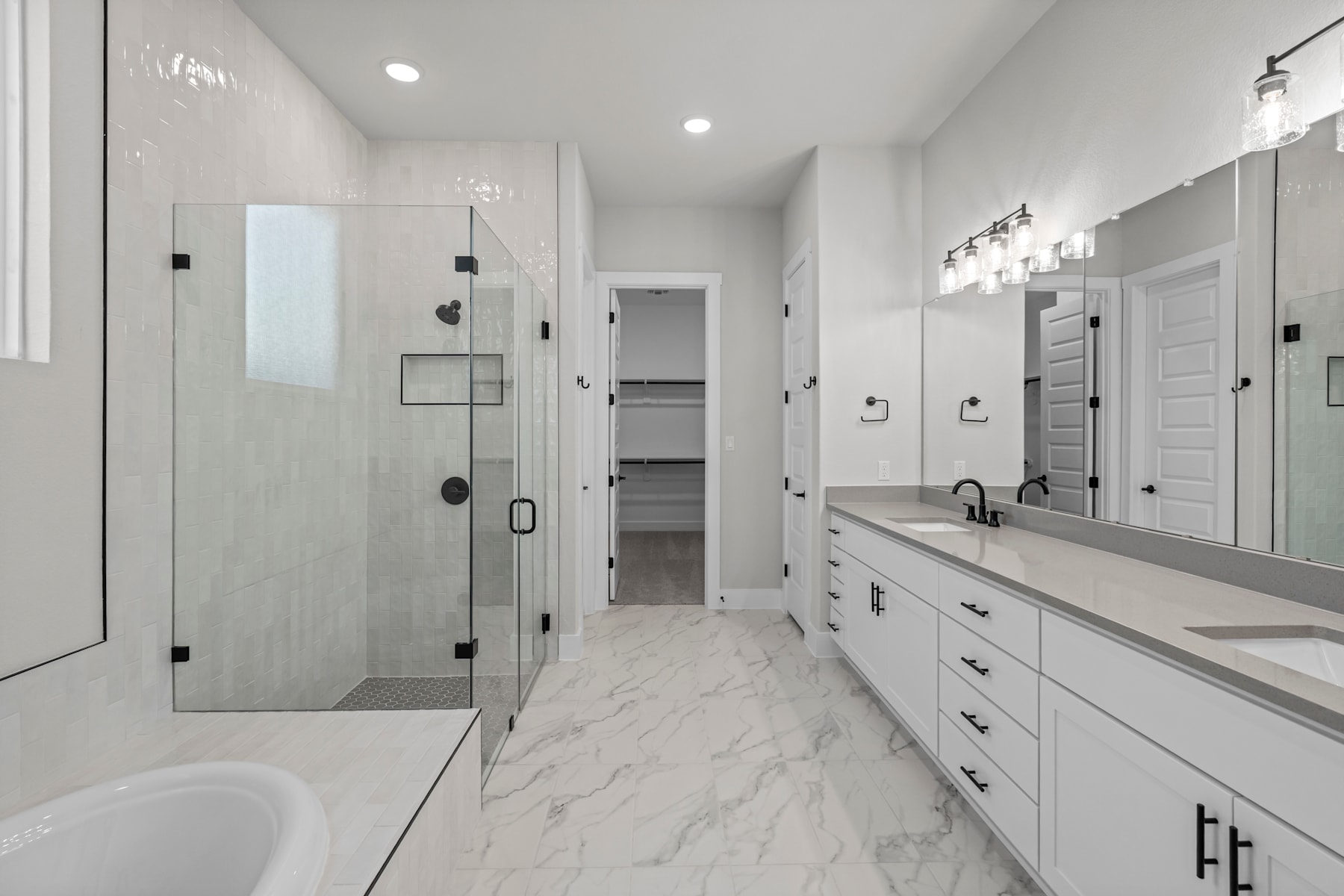 A spacious and modern bathroom with a marble-like floor, white cabinets, and a glass-enclosed shower area.