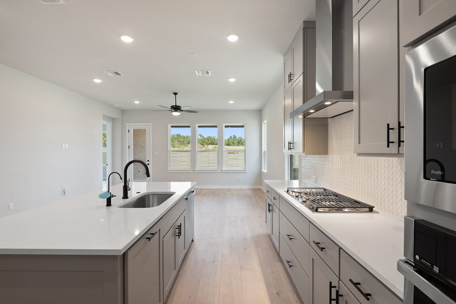 A modern, open-concept kitchen with sleek gray cabinets, a large sink, and a gas stove, set against a backdrop of large windows overlooking a scenic outdoor view.