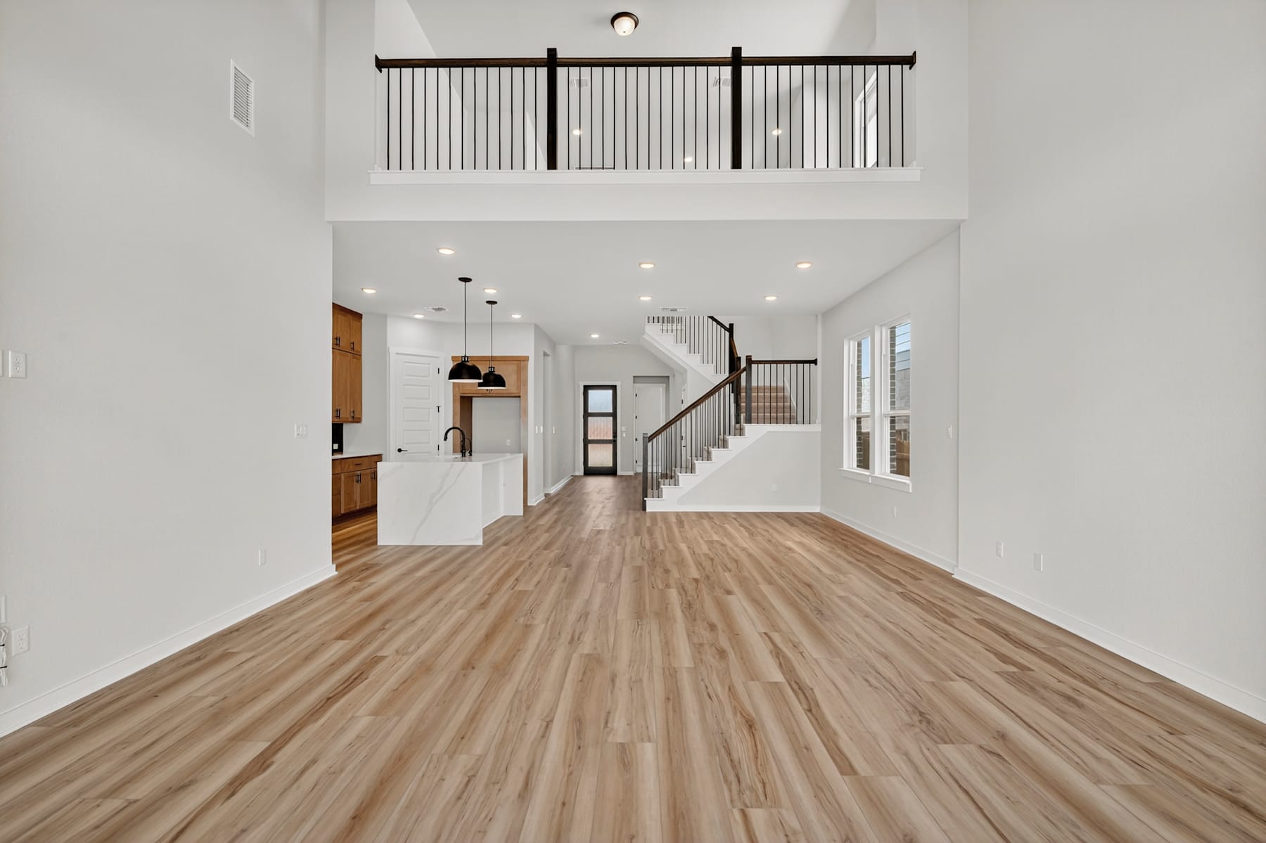 A spacious and modern interior with a wooden floor, a staircase with black railings, and a loft-like upper level visible above.