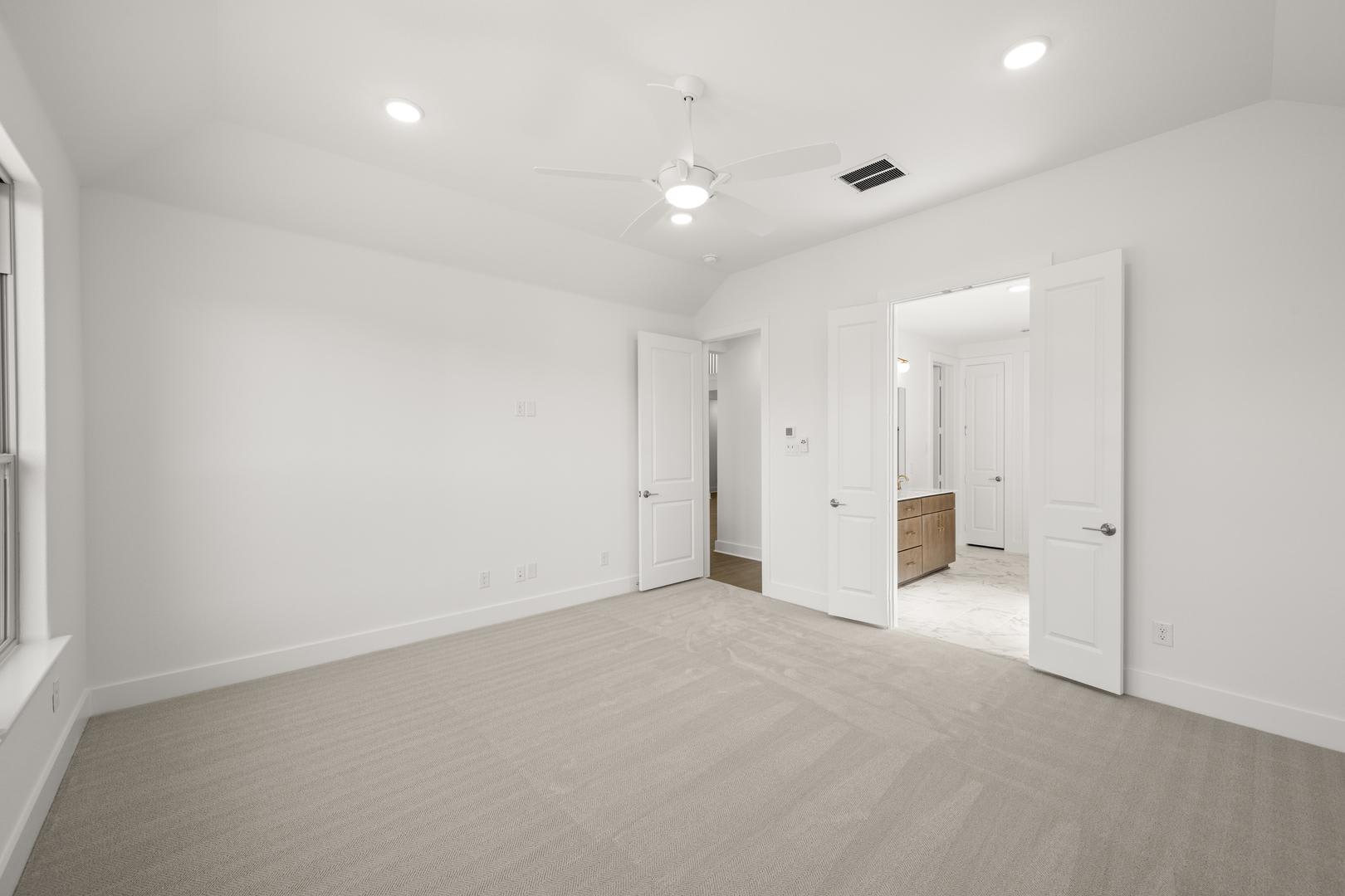 A spacious, minimalist room with white walls, a hardwood floor, and several doors leading to other areas of the space.