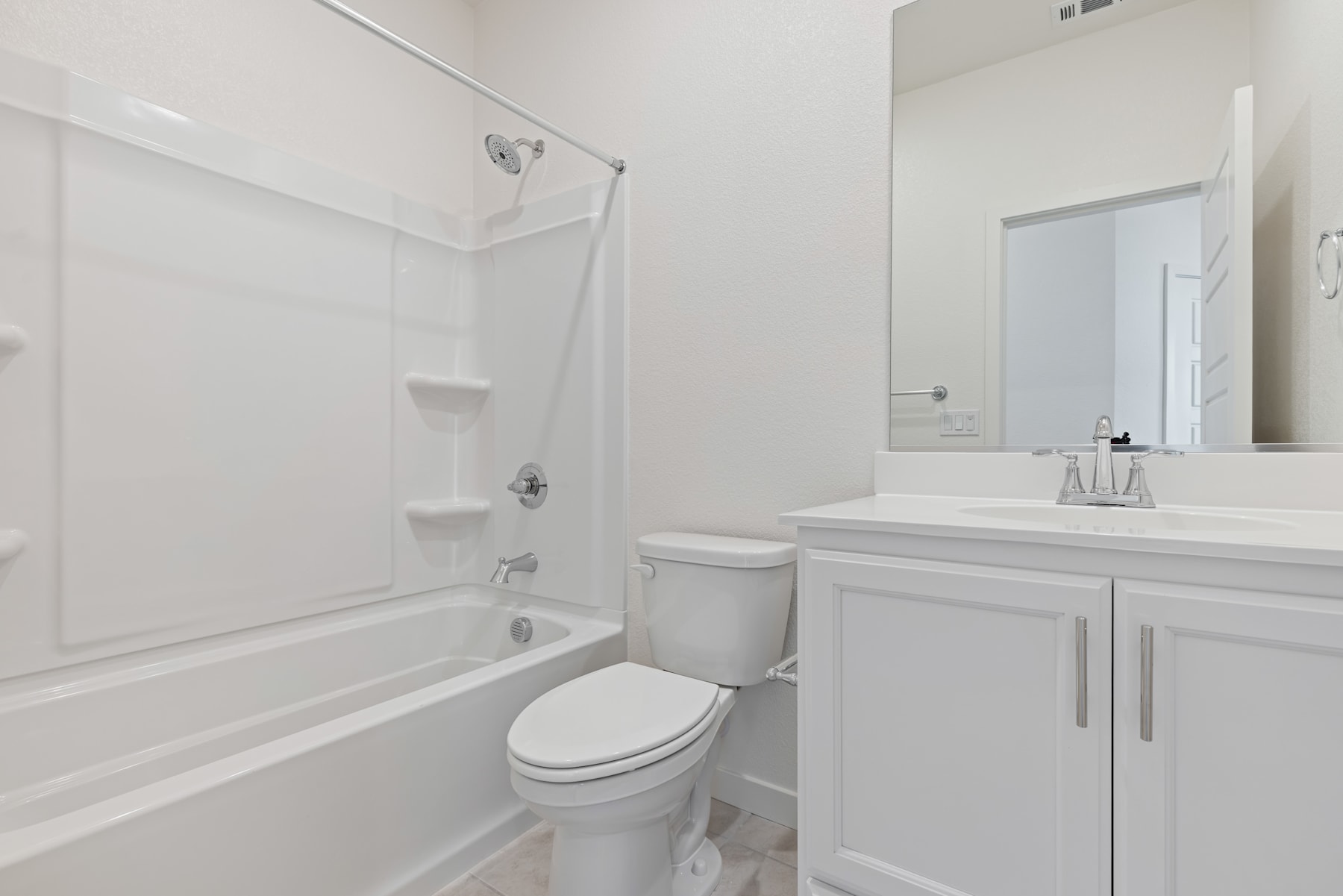 A clean, modern bathroom with a white vanity, toilet, and bathtub surrounded by white walls and tile.