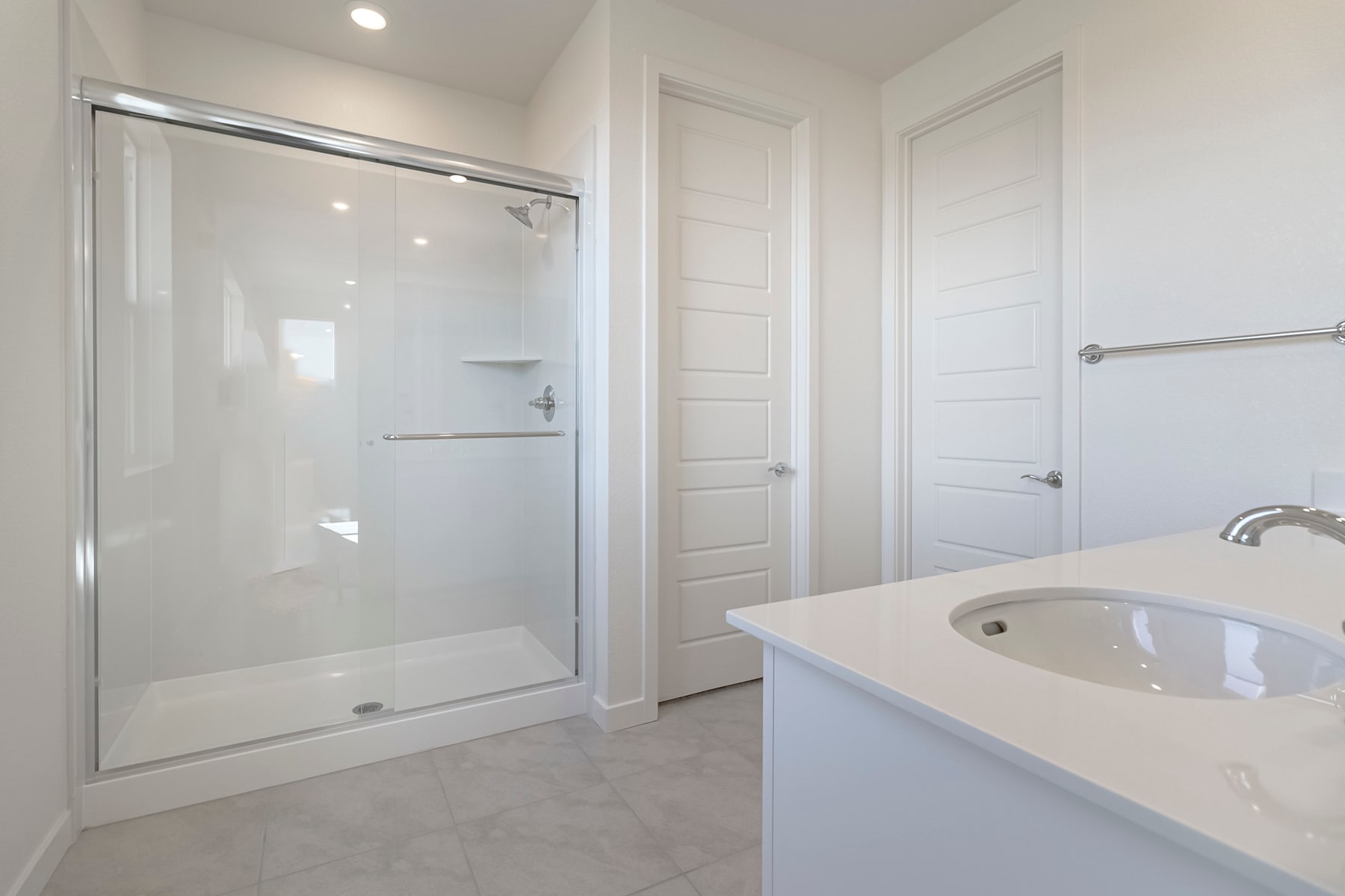 A modern, minimalist bathroom with a glass-enclosed shower, a white vanity, and a tiled floor.