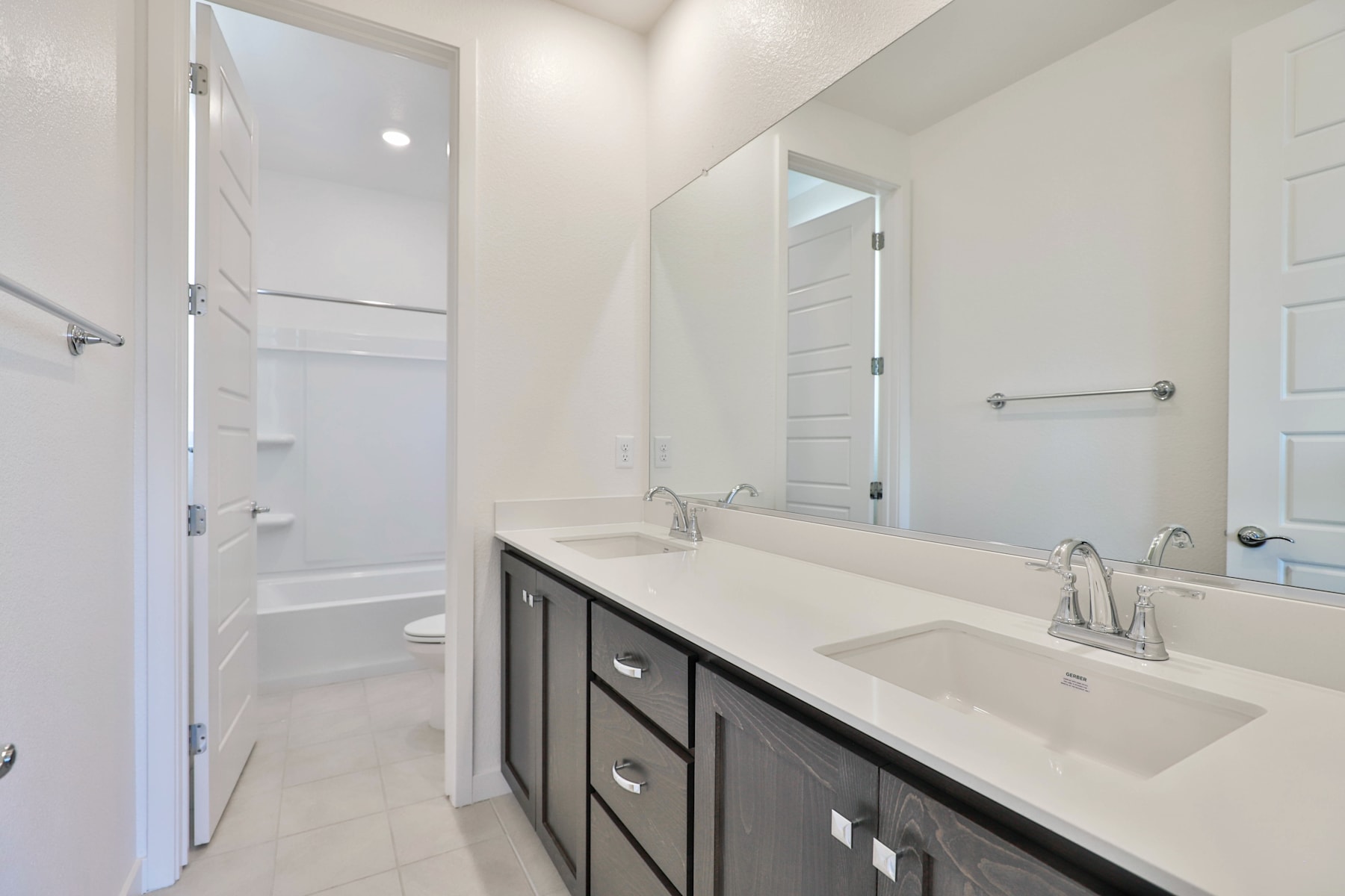 A modern bathroom with a dark vanity cabinet, a white countertop, and a mirror on the wall.