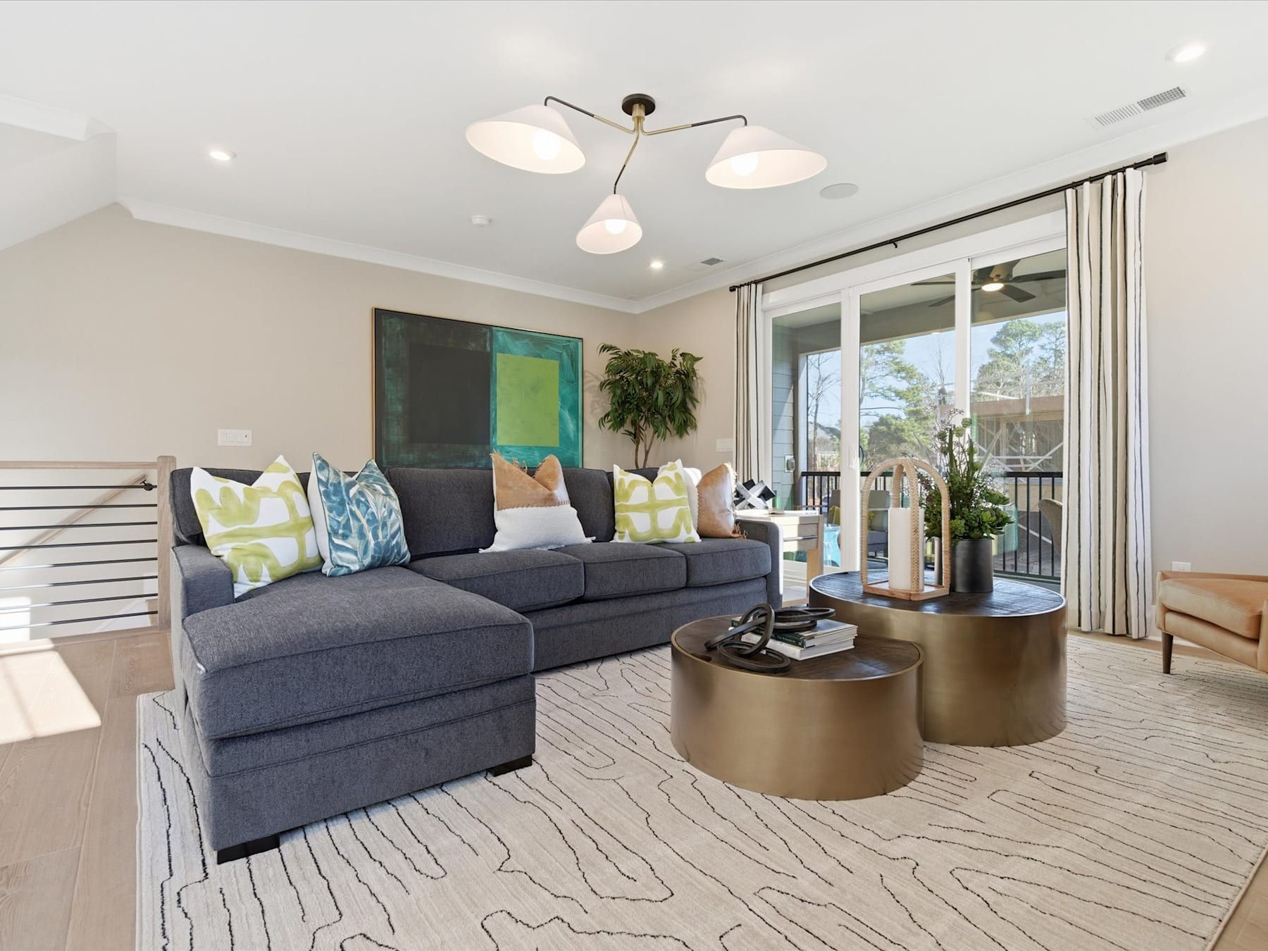 A modern and stylish living room with a comfortable gray sofa, decorative pillows, and a pair of round gold-colored side tables, set against a backdrop of large windows and a neutral-toned color scheme.
