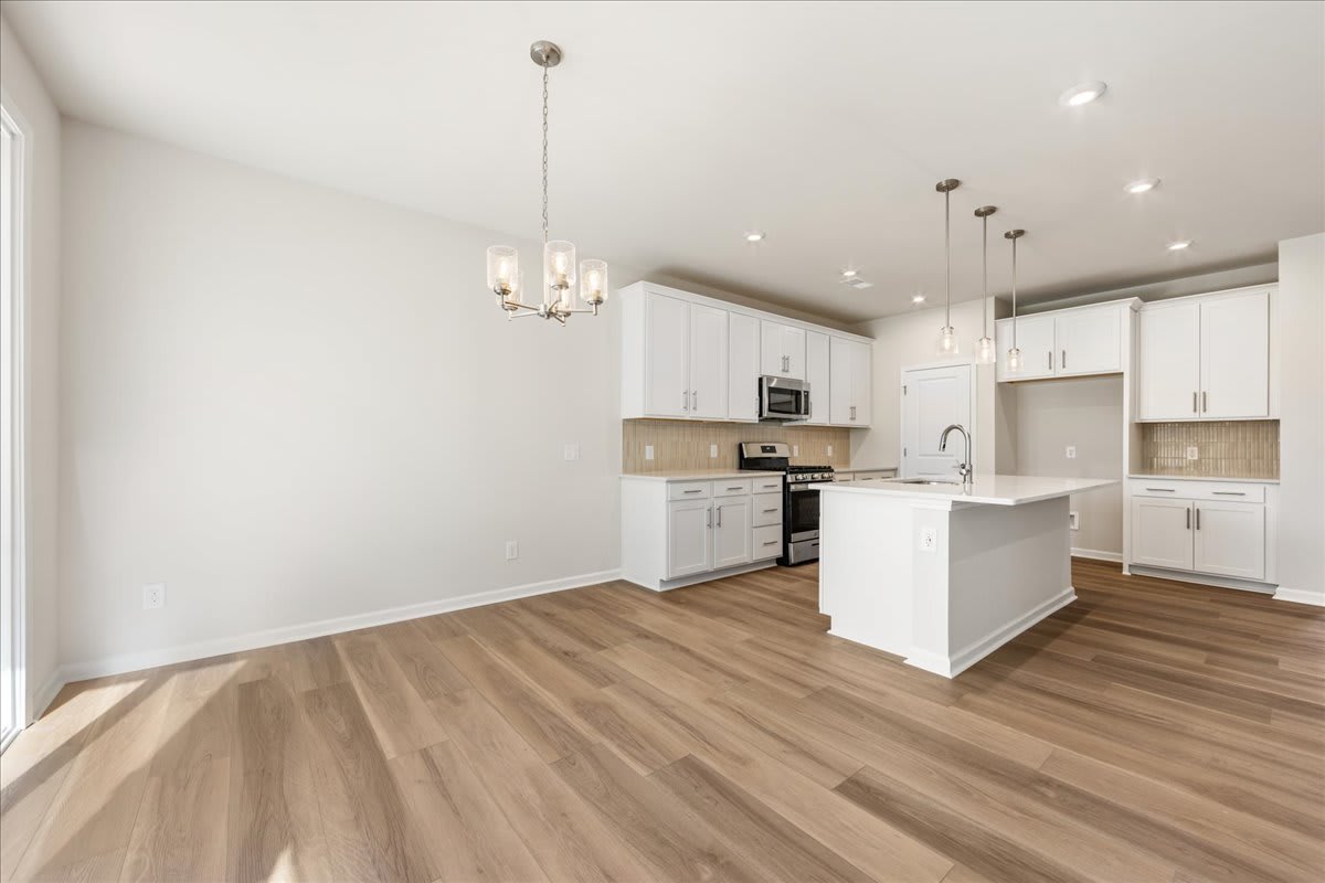 A modern, open-concept kitchen with white cabinets, stainless steel appliances, and hardwood flooring, creating a bright and spacious living environment.