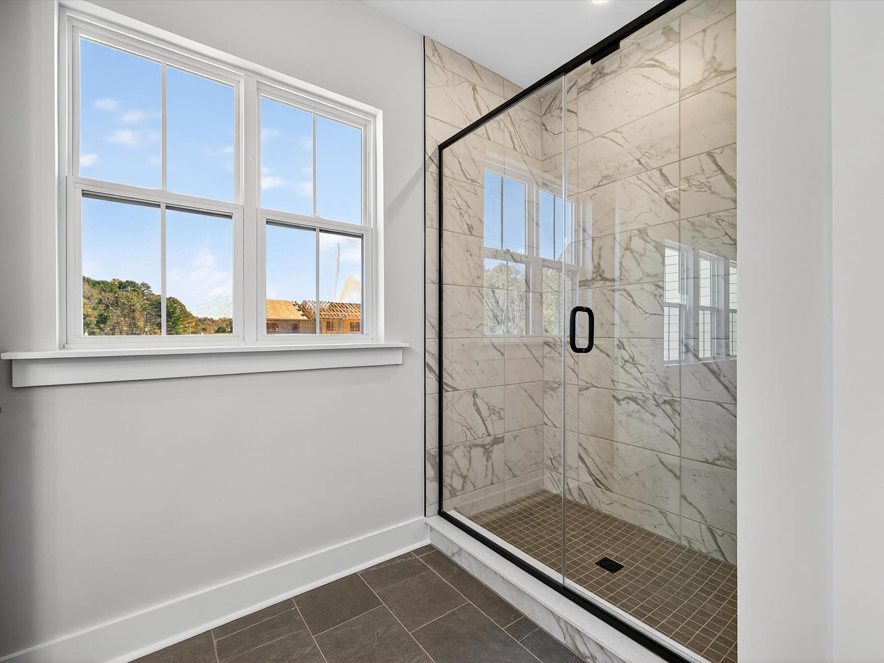 A spacious bathroom with large windows overlooking a scenic outdoor landscape, featuring a glass-enclosed shower and marble-tiled walls.