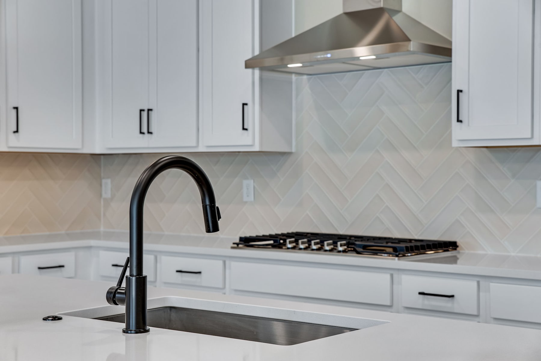 A modern kitchen with white cabinets, a stainless steel range hood, and a black faucet over a stainless steel sink.