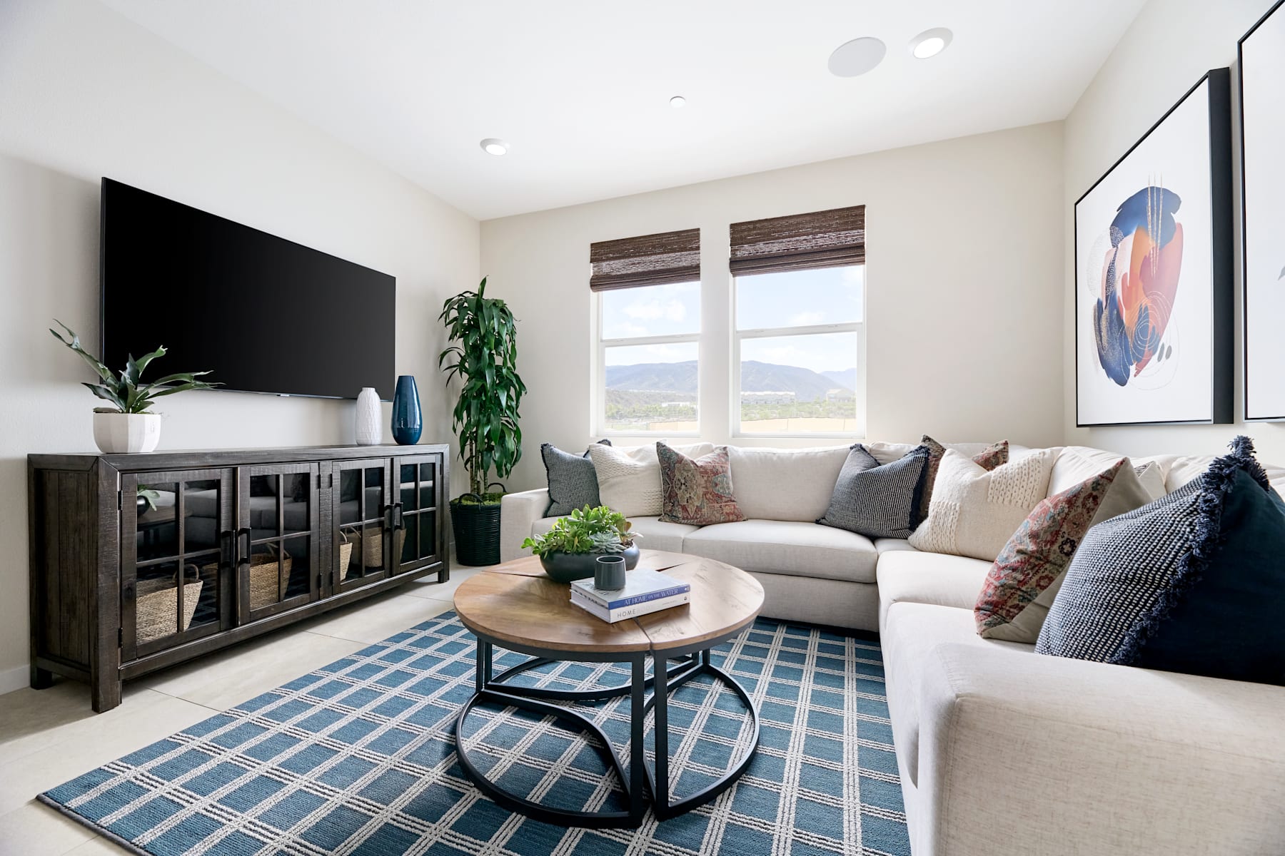 A cozy and modern living room with a comfortable sofa, a wooden coffee table, and a large TV mounted on the wall, surrounded by decorative elements and a scenic view through the windows.
