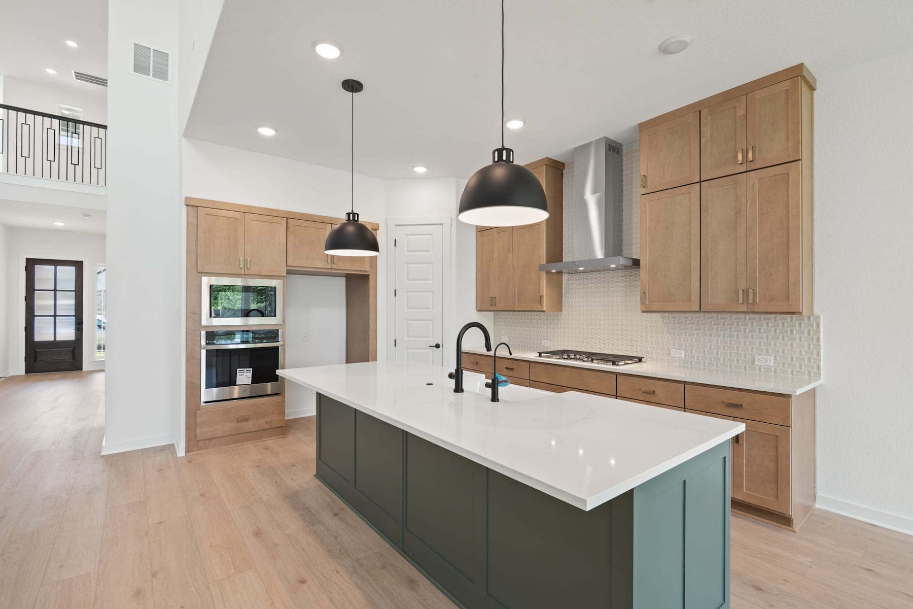 A modern, open-concept kitchen with light wood cabinets, a large island with a white countertop, and pendant lighting fixtures.