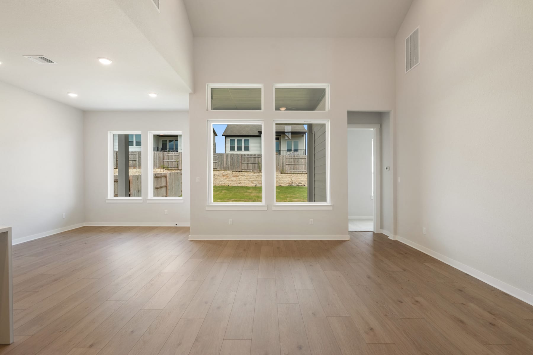 A spacious, well-lit room with large windows overlooking a grassy outdoor area, featuring hardwood floors and a minimalist, modern design.