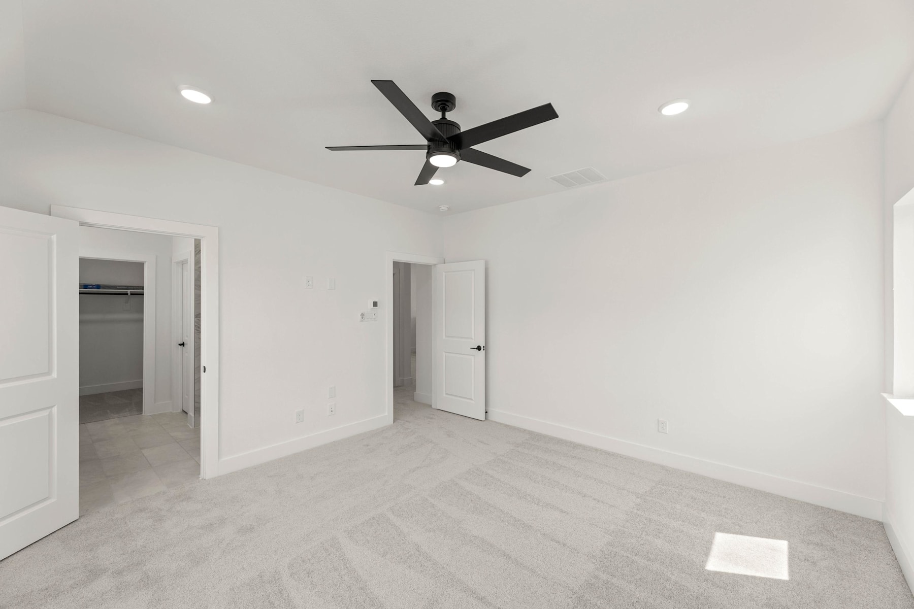A spacious, minimalist room with a ceiling fan and white walls, featuring two closed doors leading to other areas.