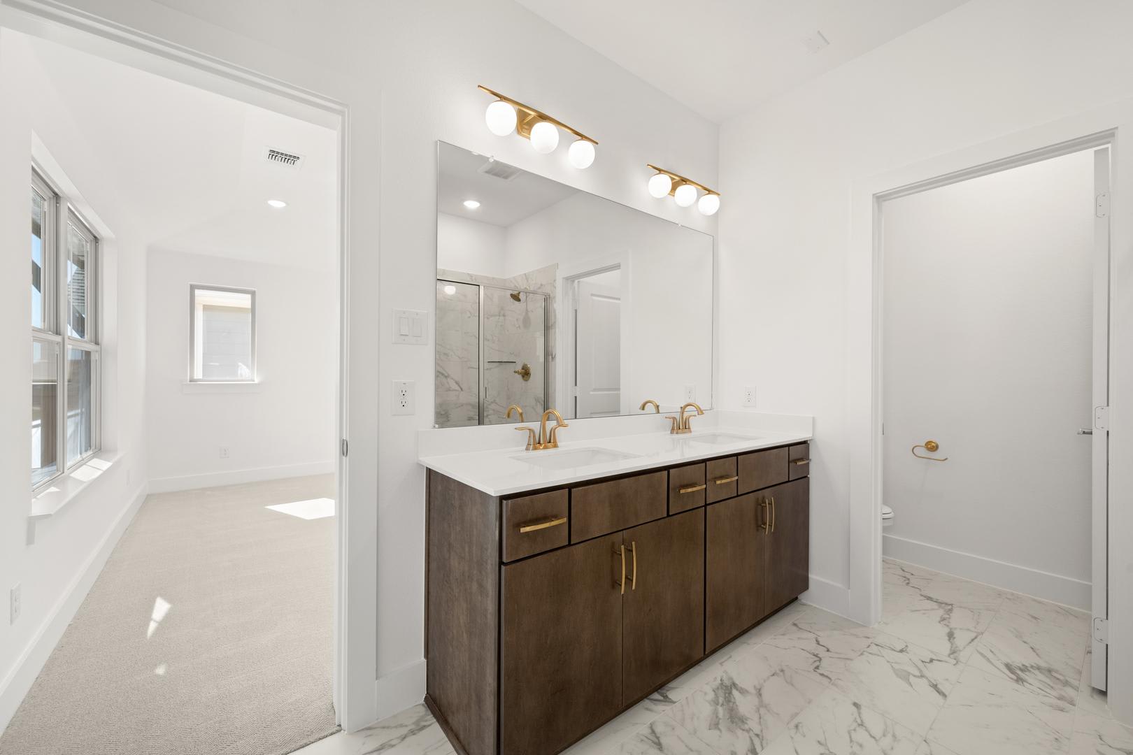 A modern and spacious bathroom with a large vanity cabinet, a marble countertop, and a well-lit mirror above it, set against a bright and airy backdrop.