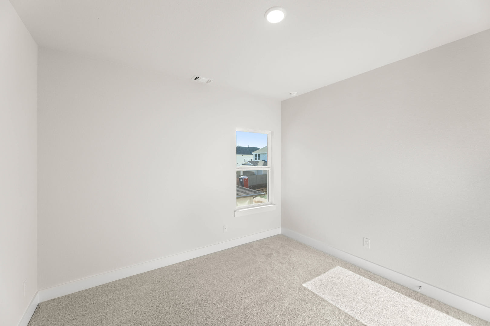 A simple, minimalist room with white walls, a small window, and a bare floor.