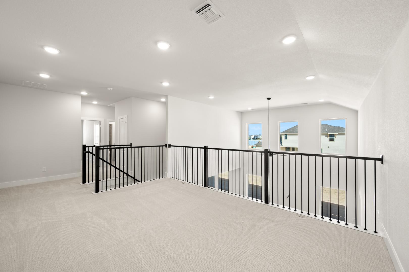 A bright, open-concept interior space with a second-floor balcony overlooking the main floor, featuring a clean, minimalist design with white walls and black metal railings.